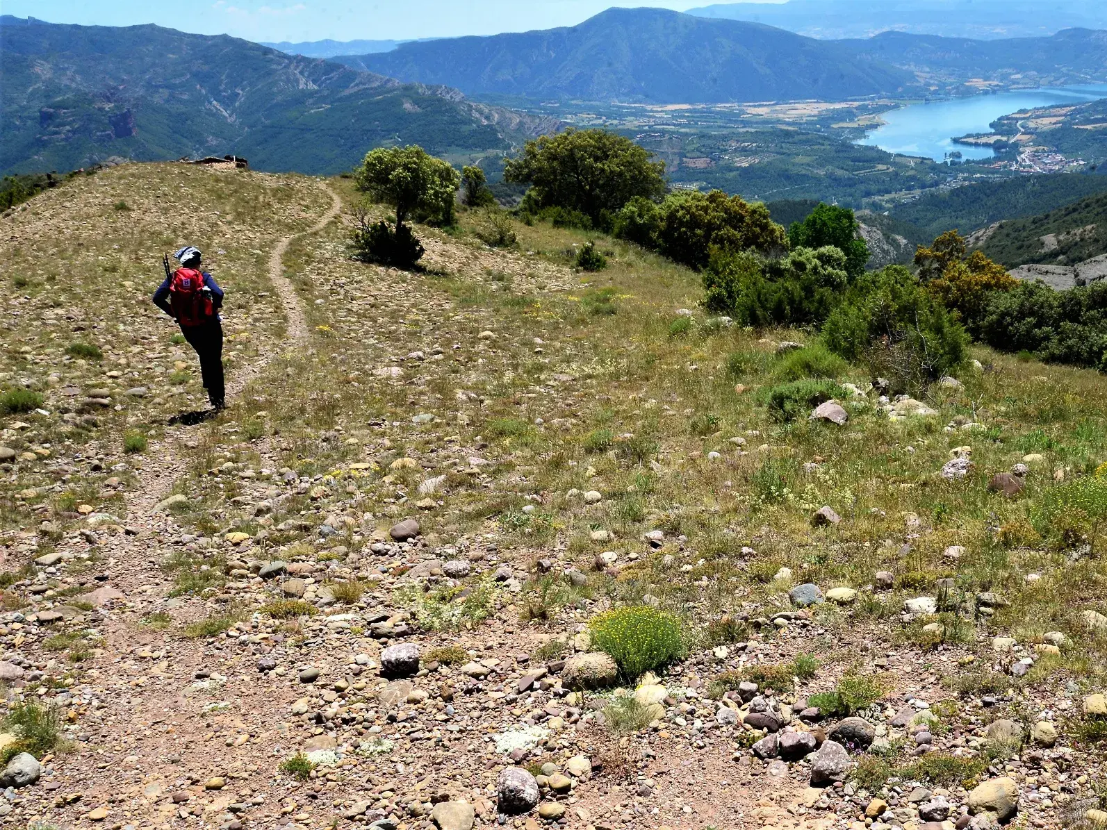 Wanderer beim Trekking auf einem Bergkamm mit weitem Ausblick über die Landschaft der südlichen Pyrenäen und einen See.
