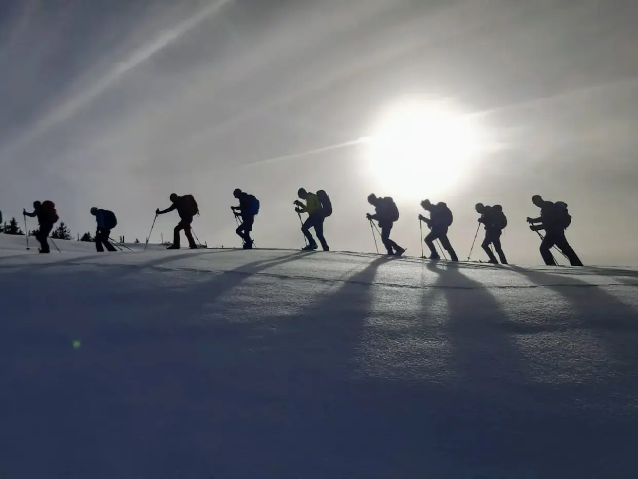 Eine Reisegruppe als Silhouetten bei einer Schneeschuhwanderung auf einem Schneefeld in den Kitzbüheler Alpen im Gegenlicht.