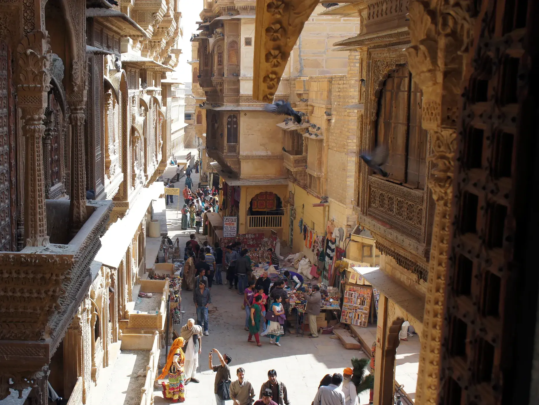 Blick von einem Haveli auf eine belebte Gasse mit Marktständen und Menschen in der goldenen Stadt Jaisalmer in Rajasthan.