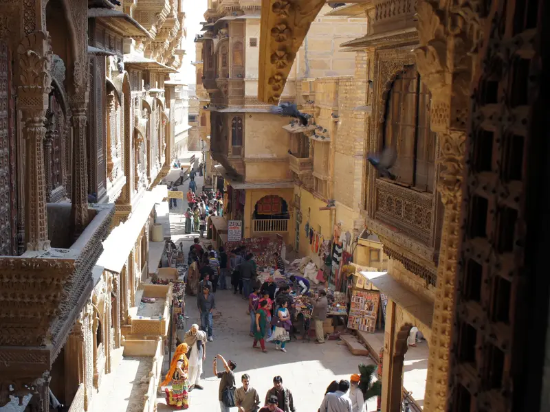 Blick von einem Haveli auf eine belebte Gasse mit Marktständen und Menschen in der goldenen Stadt Jaisalmer in Rajasthan.