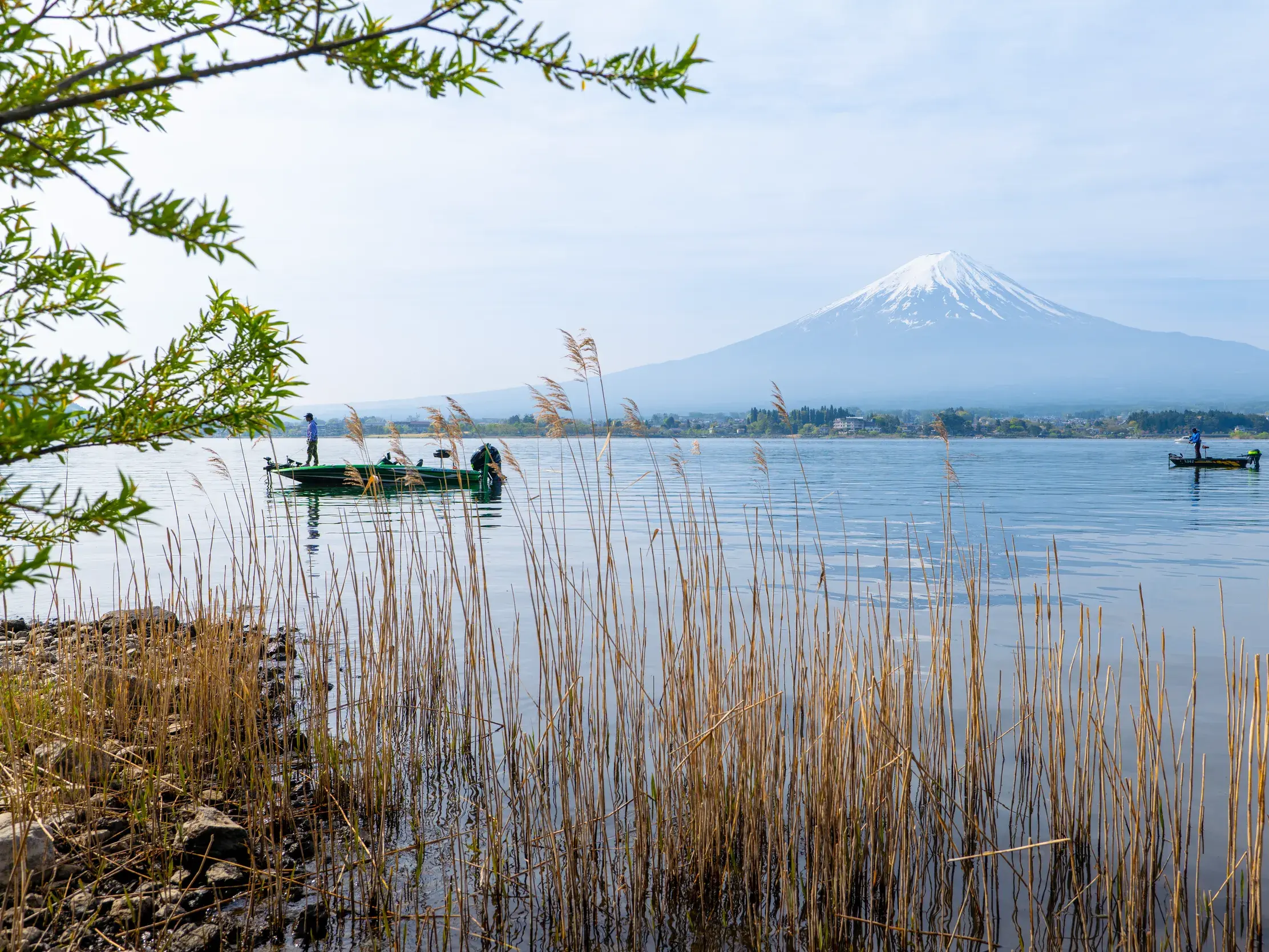 Malerischer Ausblick über den Kawaguchi-See mit Fischerbooten auf den schneebedeckten heiligen Berg Fuji-san in Japan.