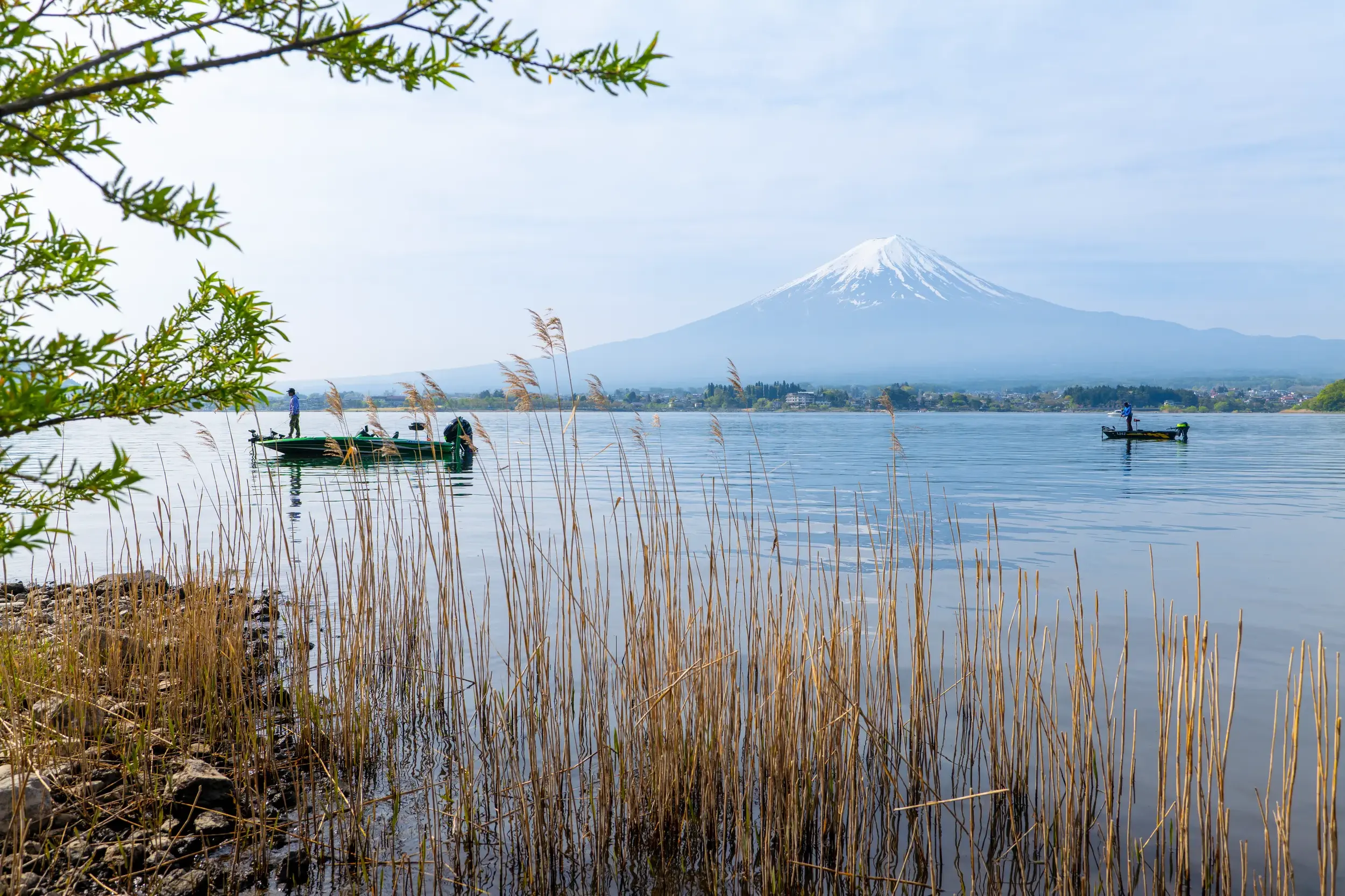Malerischer Ausblick über den Kawaguchi-See mit Fischerbooten auf den schneebedeckten heiligen Berg Fuji-san in Japan.
