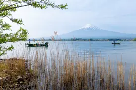 Malerischer Ausblick über den Kawaguchi-See mit Fischerbooten auf den schneebedeckten heiligen Berg Fuji-san in Japan.