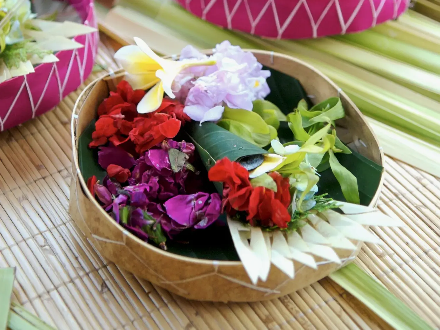 Nahaufnahme einer traditionellen balinesischen Opfergabe, Canang Sari, mit bunten Blüten und Blättern in einem geflochtenen Korb.