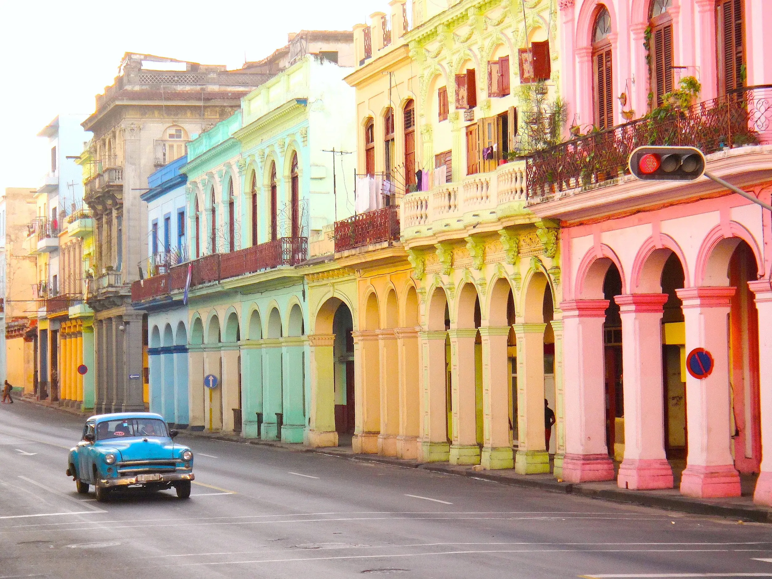 Ein blauer Oldtimer fährt durch eine Straße in Havannas Altstadt, gesäumt von farbenfrohen Kolonialgebäuden mit Arkaden.