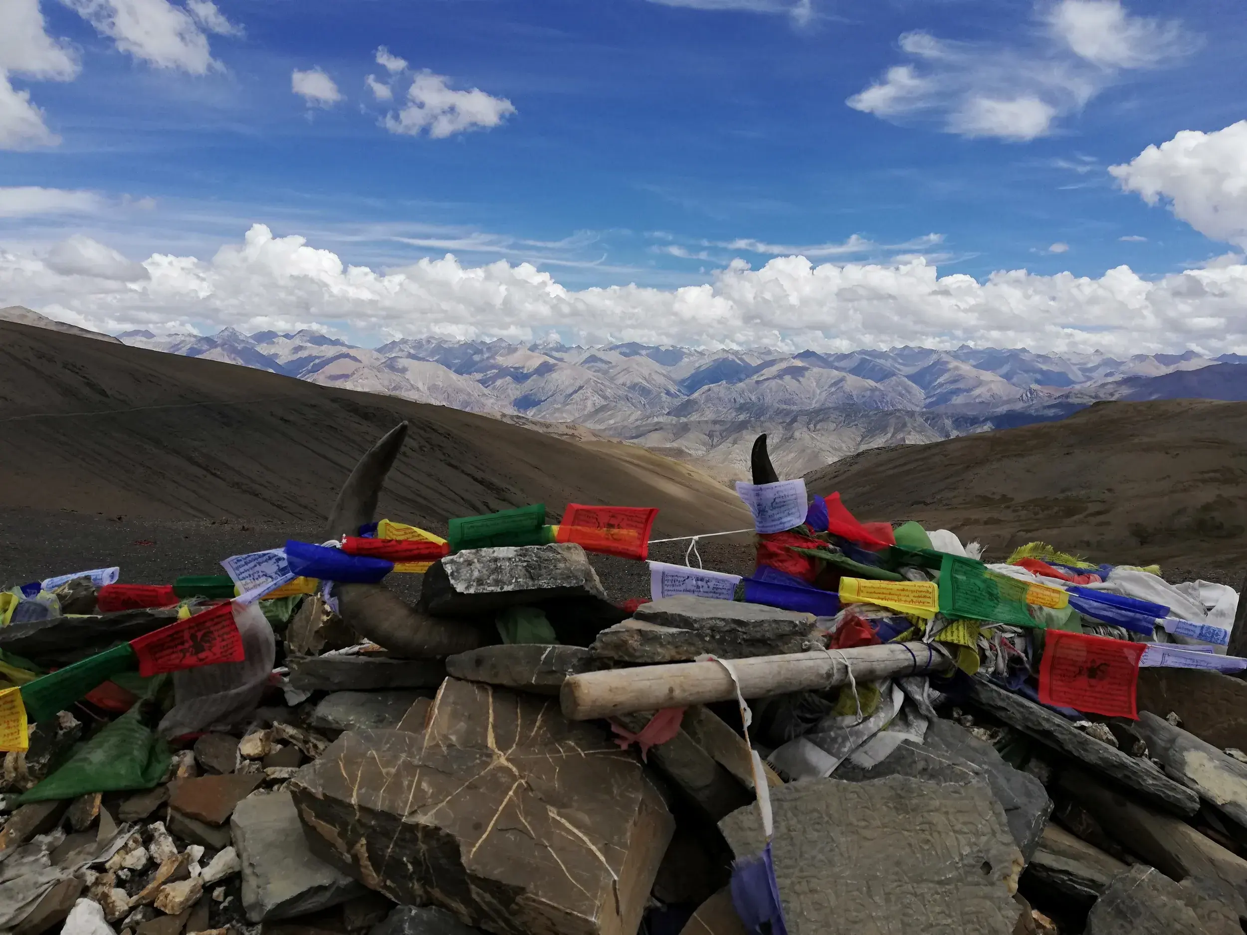 Steinhaufen mit bunten, tibetischen Gebetsfahnen auf einer Passhöhe im Dolpo mit Weitblick über die Bergketten Nepals.