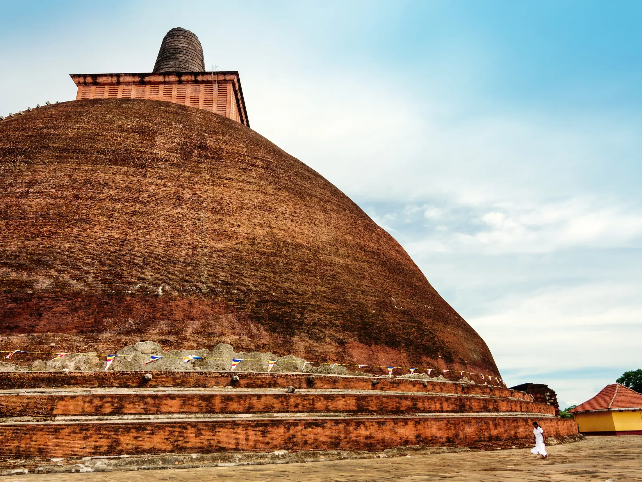 Eine Person in weißer Kleidung geht an der gewaltigen, aus Ziegeln erbauten Jetavanaramaya-Stupa in Anuradhapura vorbei.