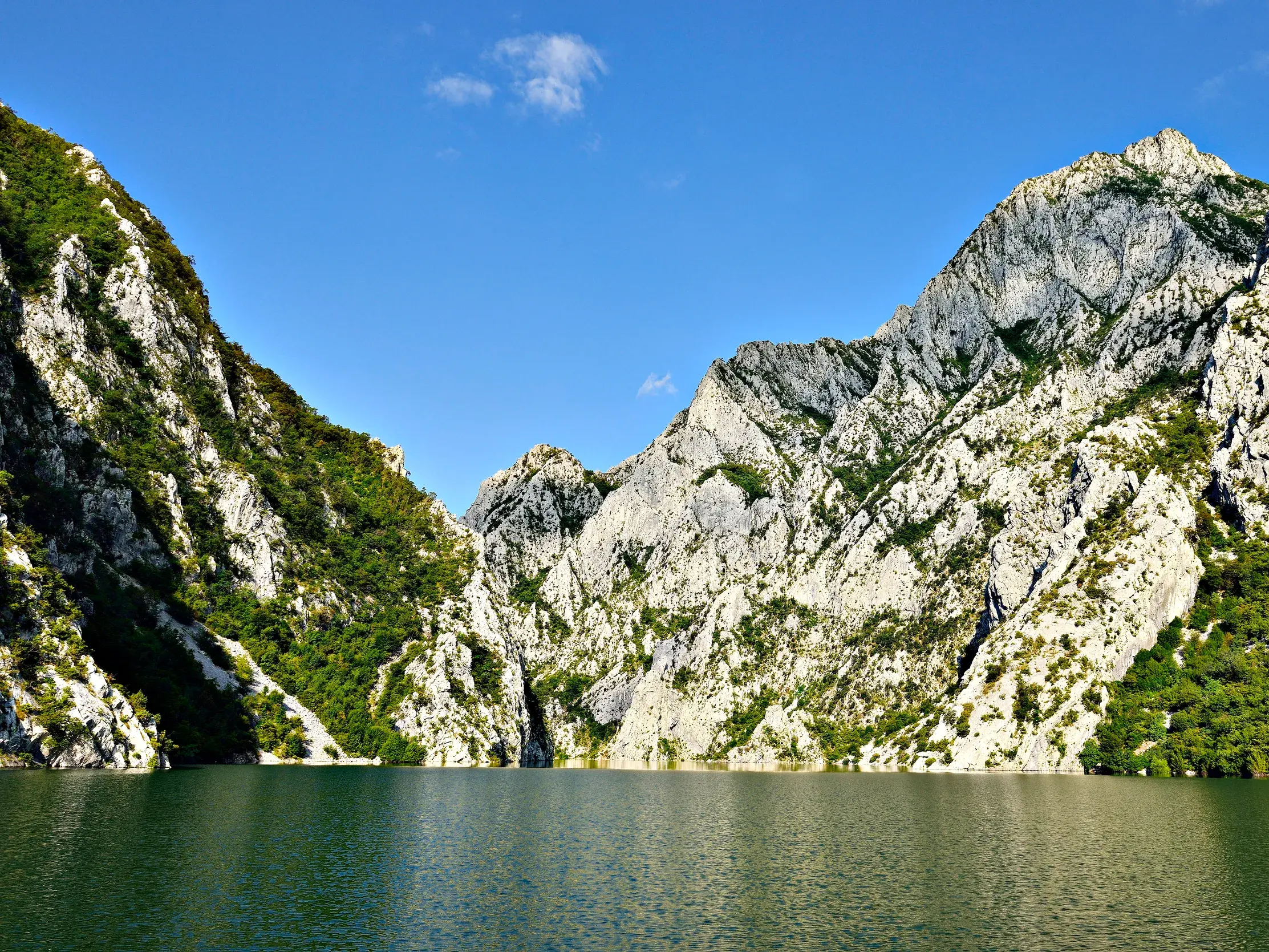 Fährfahrt auf dem Koman-Stausee durch die imposante Drin-Schlucht mit steilen, bewachsenen Felswänden in Albanien.