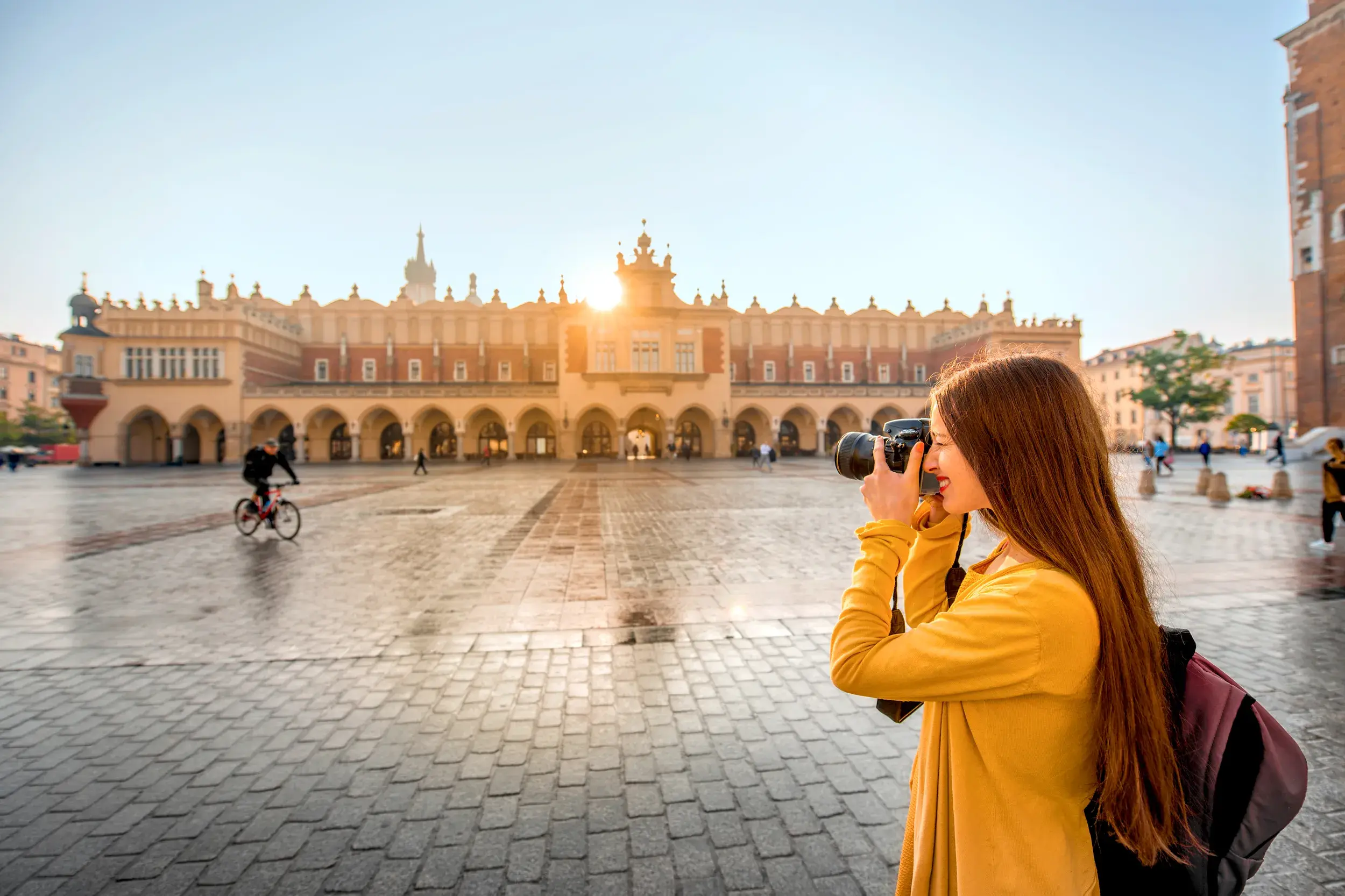 Junge Frau macht ein Foto der historischen Renaissance-Tuchhallen auf dem Marktplatz von Krakau im warmen Morgenlicht.