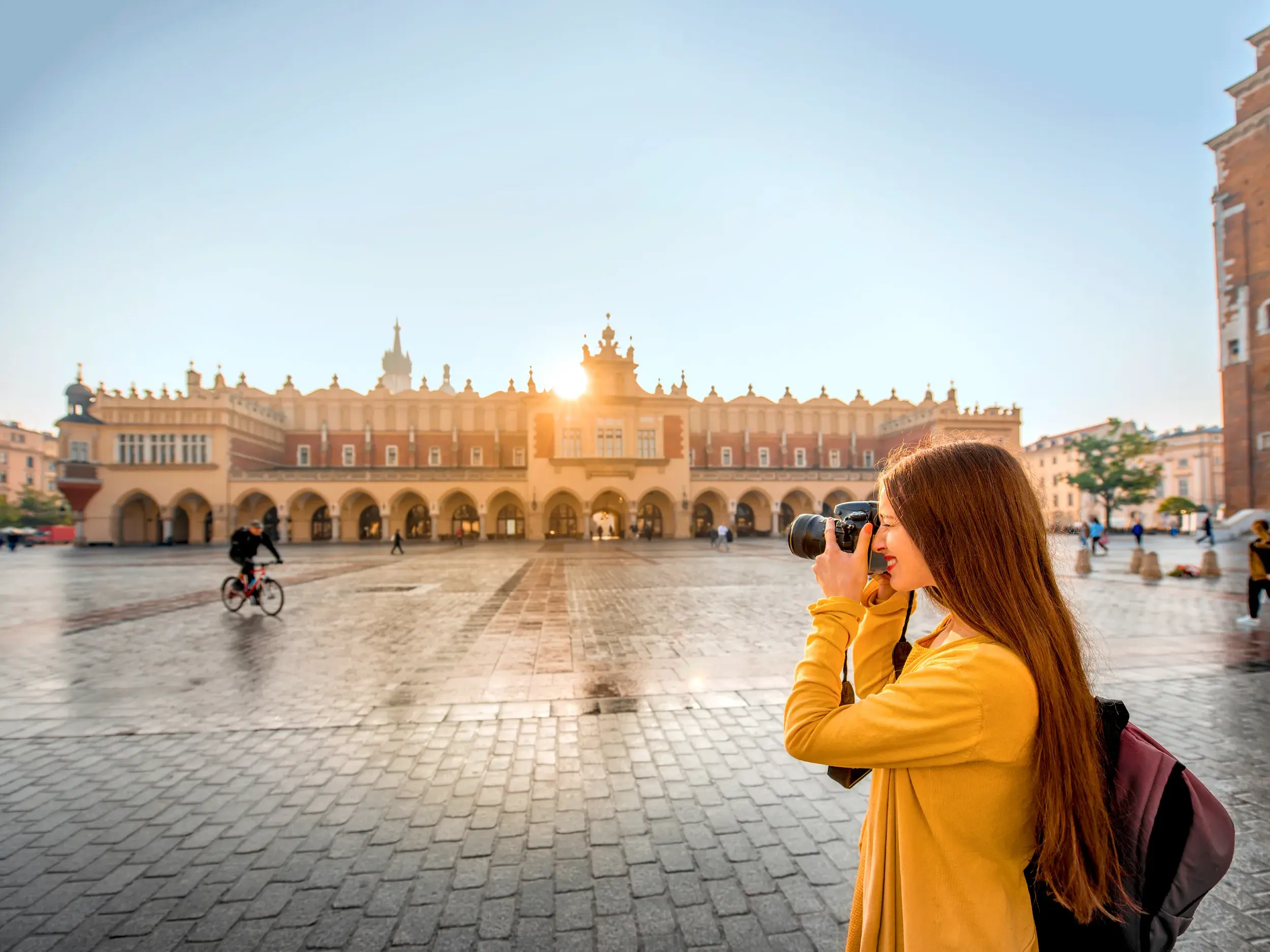 Junge Frau macht ein Foto der historischen Renaissance-Tuchhallen auf dem Marktplatz von Krakau im warmen Morgenlicht.