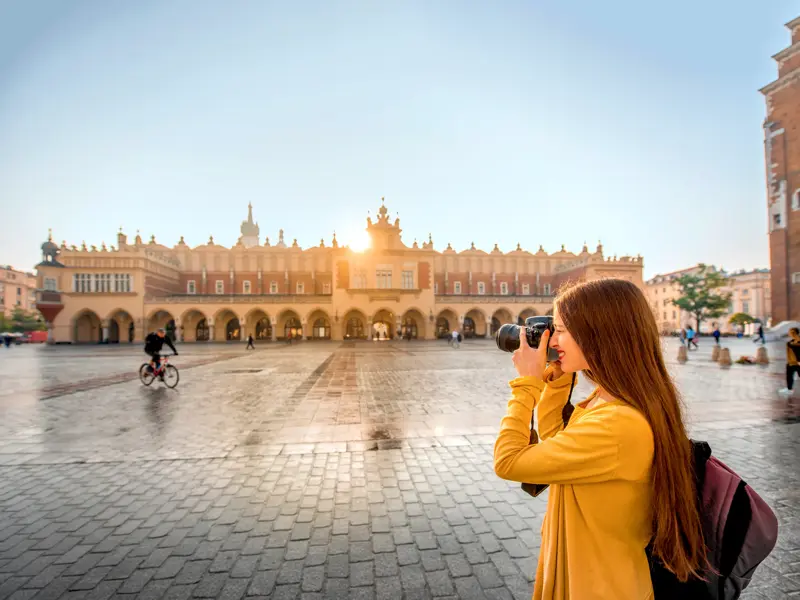 Junge Frau macht ein Foto der historischen Renaissance-Tuchhallen auf dem Marktplatz von Krakau im warmen Morgenlicht.