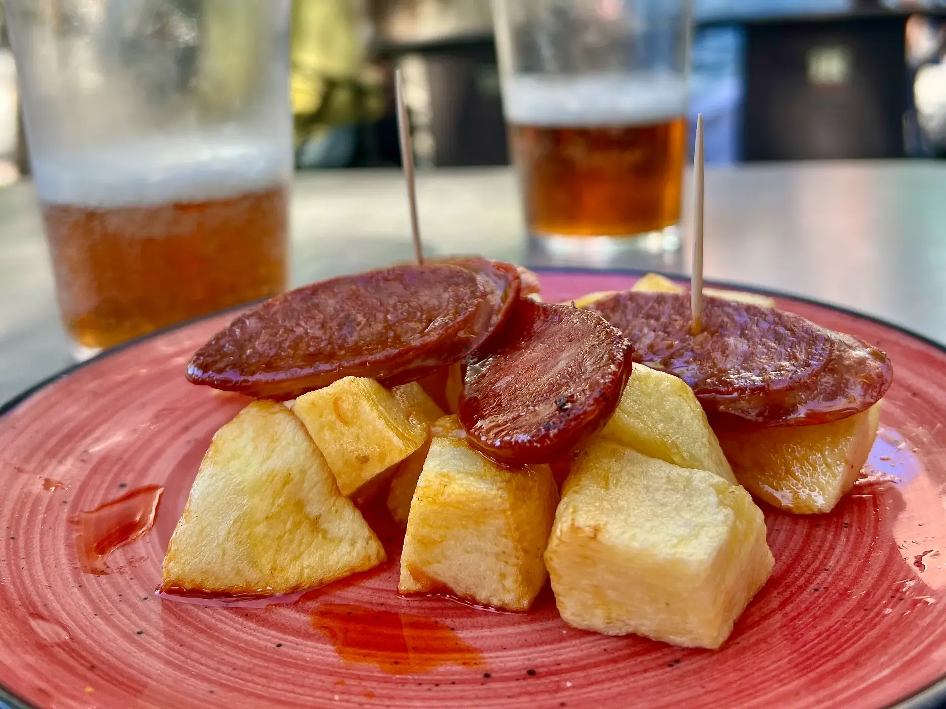 Nahaufnahme einer kastilischen Spezialität: würzige Chorizo auf Kartoffelwürfeln, serviert mit Bier in einer spanischen Bar.
