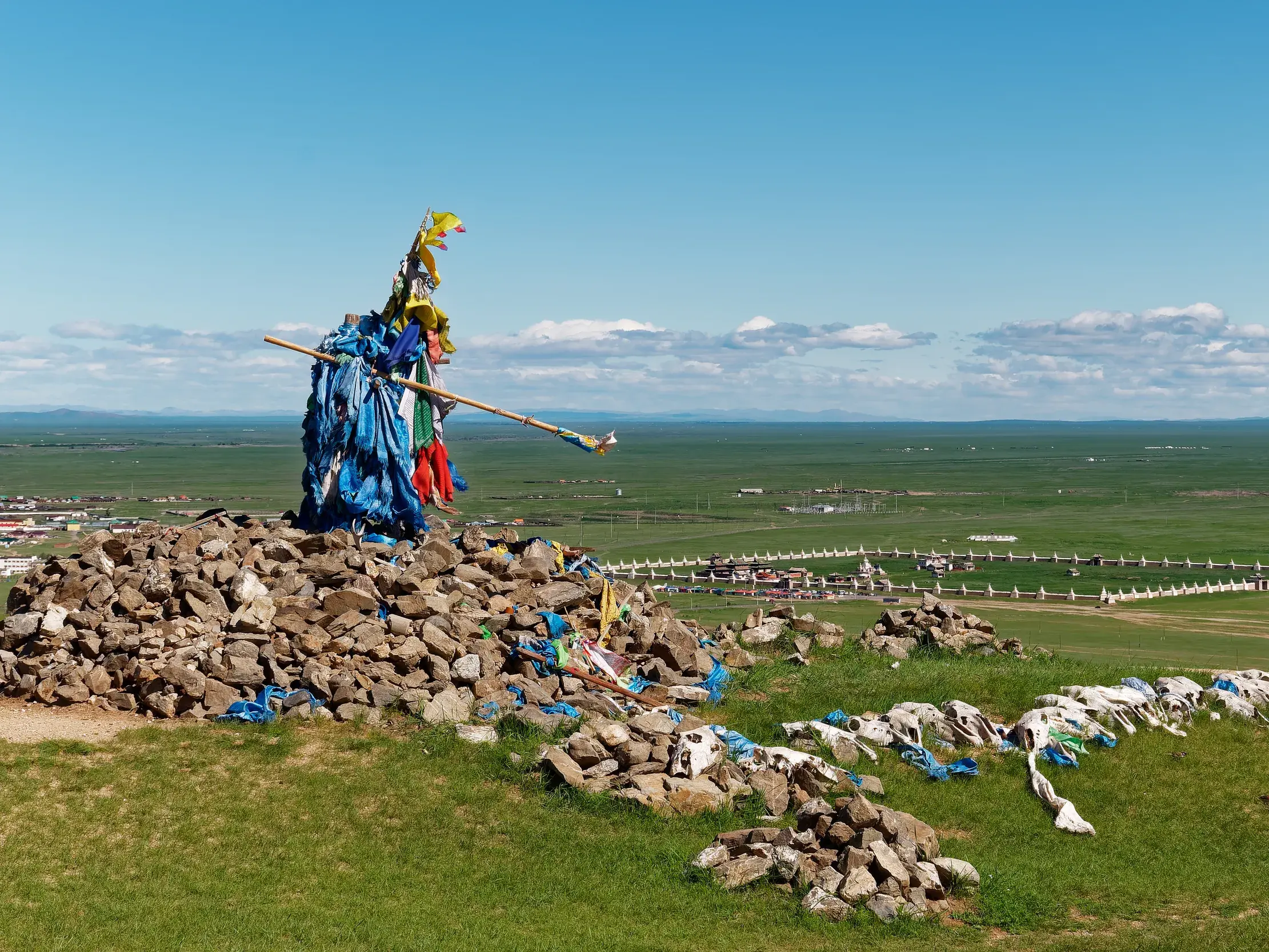 Panoramablick von einem Obo-Steinhaufen mit bunten Fahnen auf die grüne Steppe und das Erdene-Zuu-Kloster in Karakorum.