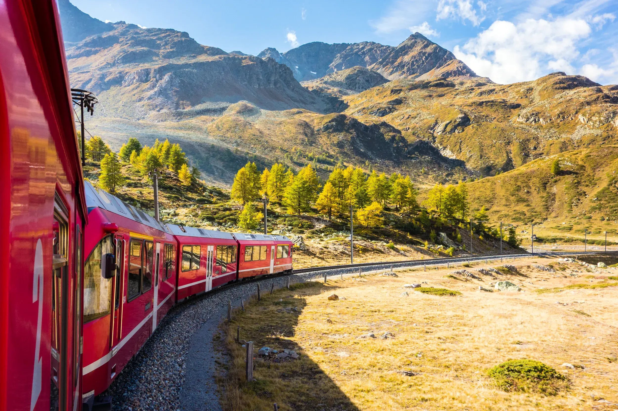 Der rote Bernina Express der Rhätischen Bahn fährt auf einer kurvigen Strecke über den sonnigen Berninapass in Graubünden.
