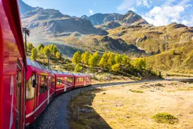 Der rote Bernina Express der Rhätischen Bahn fährt auf einer kurvigen Strecke über den sonnigen Berninapass in Graubünden.