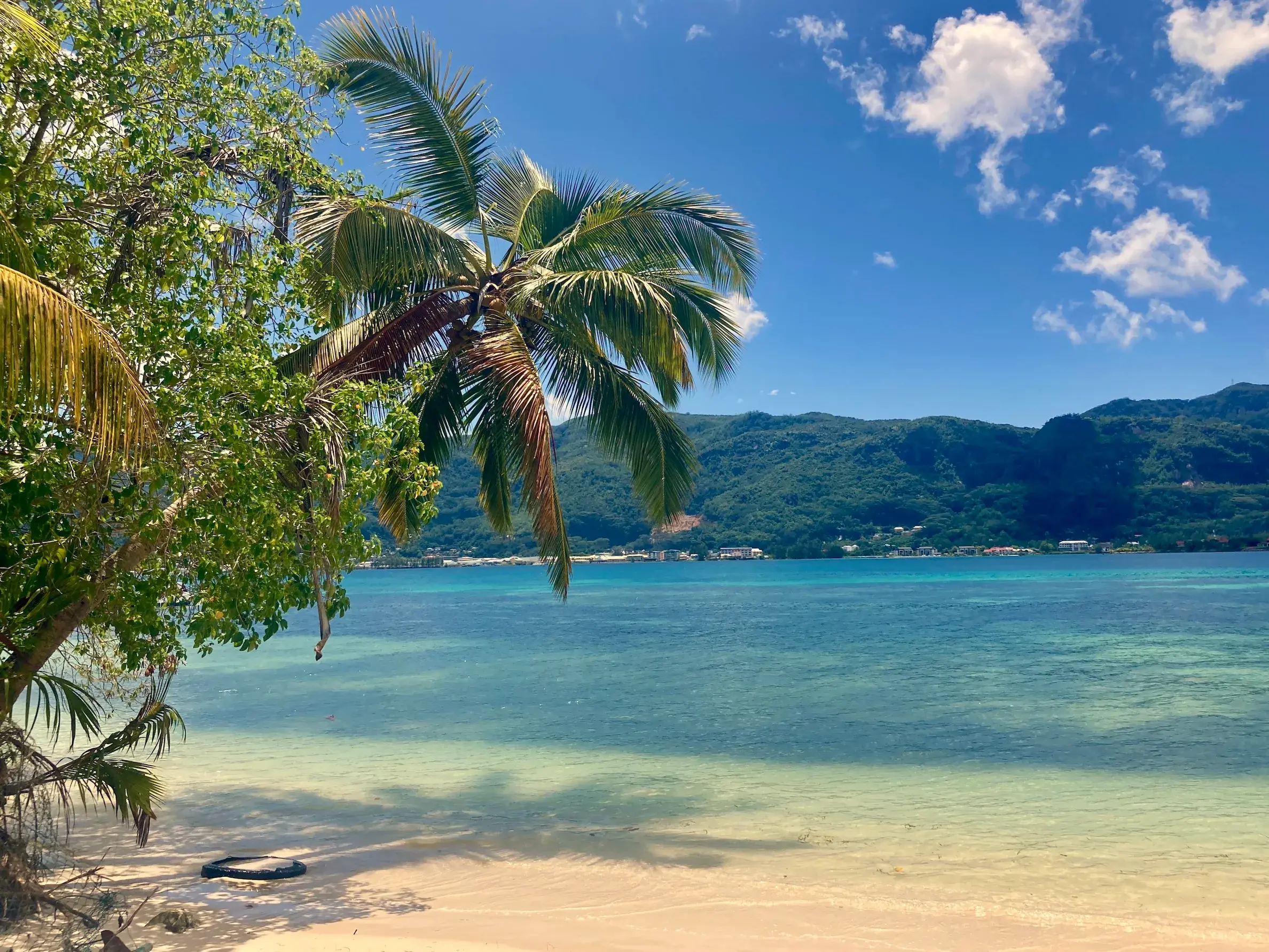 Blick von einem Sandstrand auf Cerf Island über das türkise Meer auf die bergige Küste von Mahé auf den Seychellen.