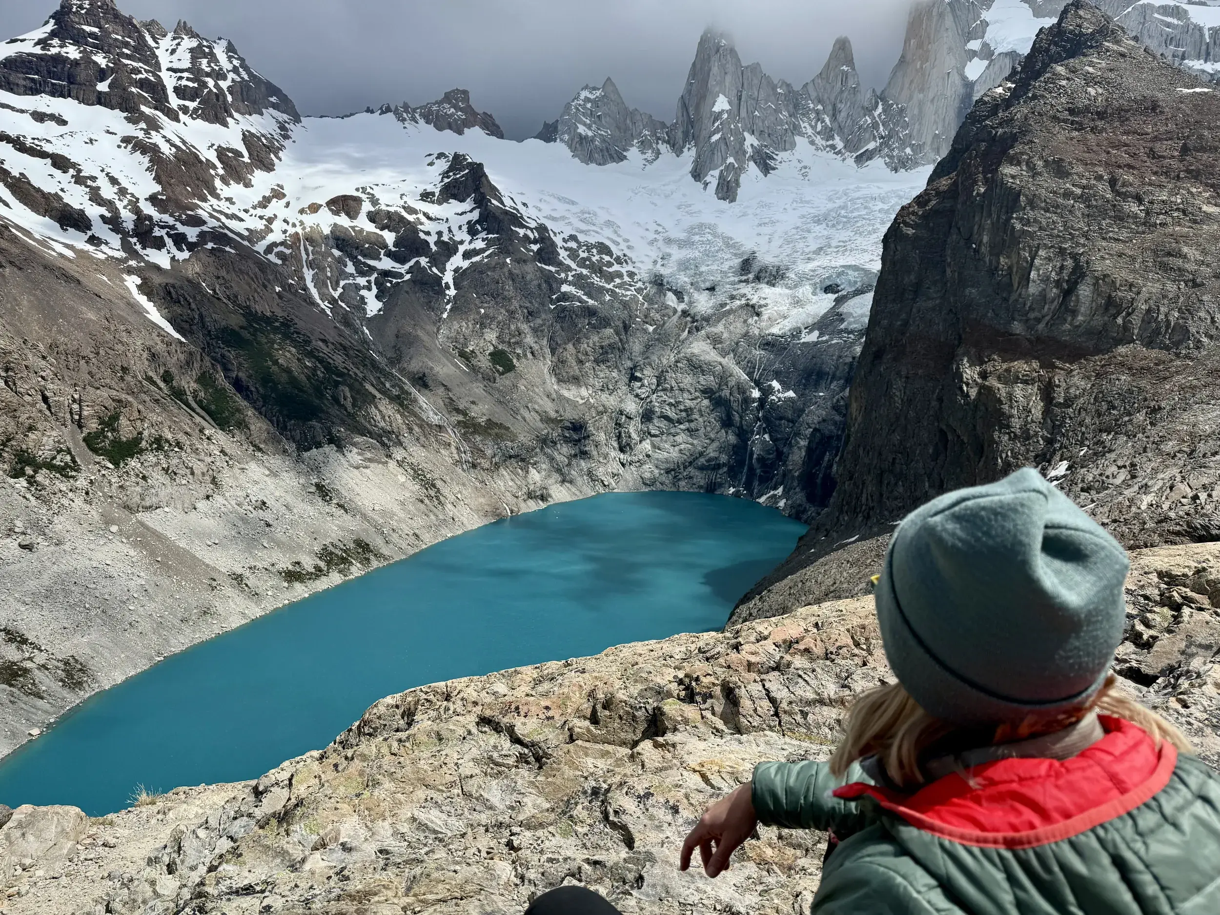 Eine Wanderin genießt den Ausblick auf die türkisfarbene Laguna de los Tres vor der Kulisse der schneebedeckten Anden in Argentinien.
