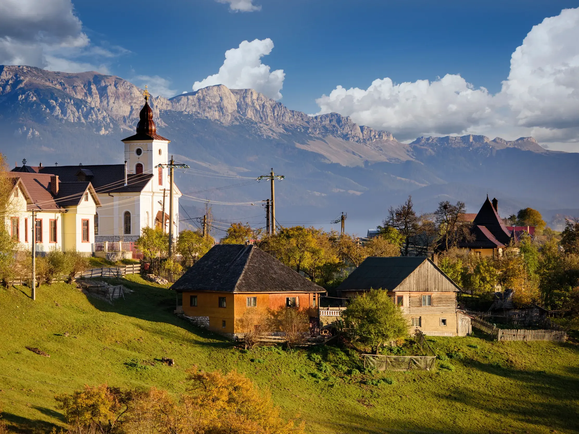 Eine Kirche und traditionelle Holzhäuser im Bergdorf Magura vor der Kulisse der Karpaten auf einer Wanderreise in Siebenbürgen.