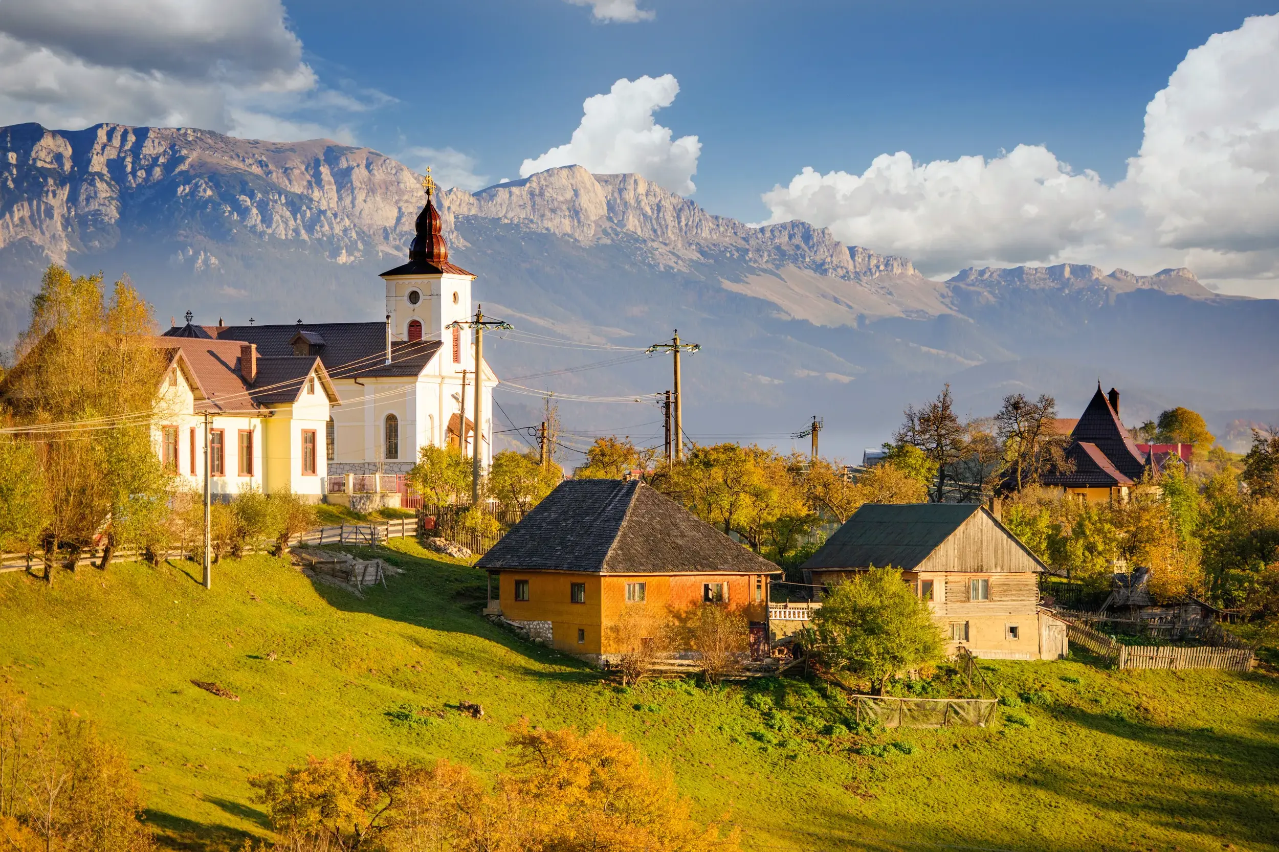 Kirche und traditionelle Holzhäuser im Bergdorf Magura vor der Kulisse des Piatra Craiului-Gebirges in Siebenbürgen.