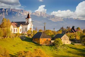 Kirche und traditionelle Holzhäuser im Bergdorf Magura vor der Kulisse des Piatra Craiului-Gebirges in Siebenbürgen.