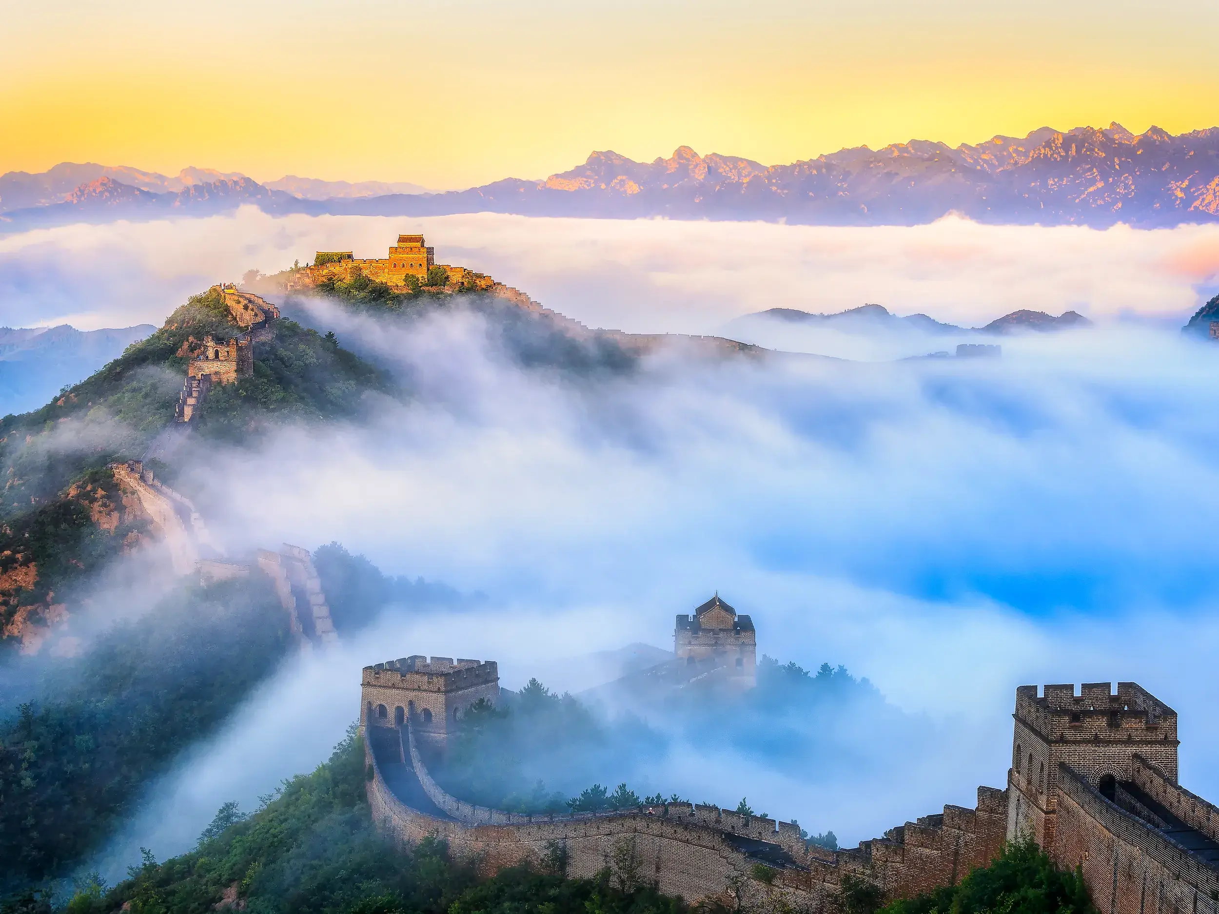 Die Große Mauer Chinas (UNESCO-Welterbe) schlängelt sich bei Sonnenaufgang majestätisch durch nebelverhangene Berge.