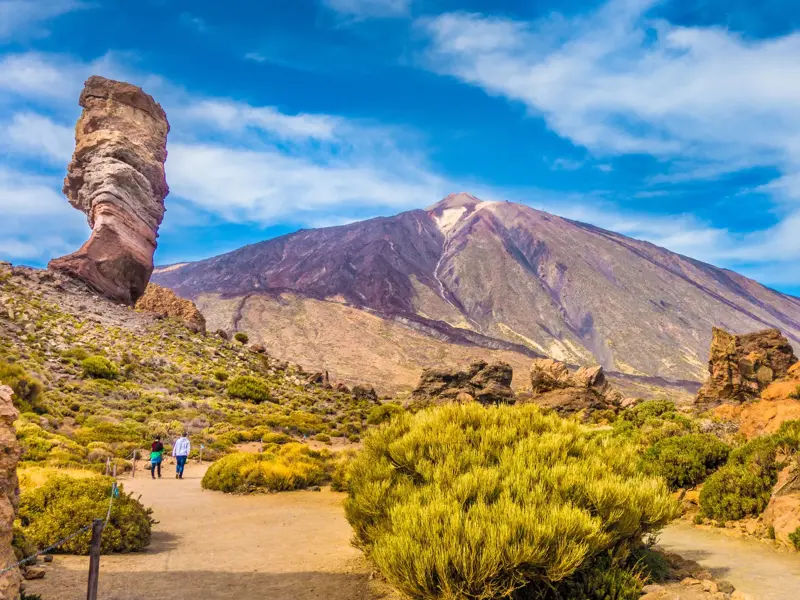 Zwei Wanderer im Teide Nationalpark auf Teneriffa mit Blick auf die Felsformation Roque Cinchado und den Vulkan Teide.