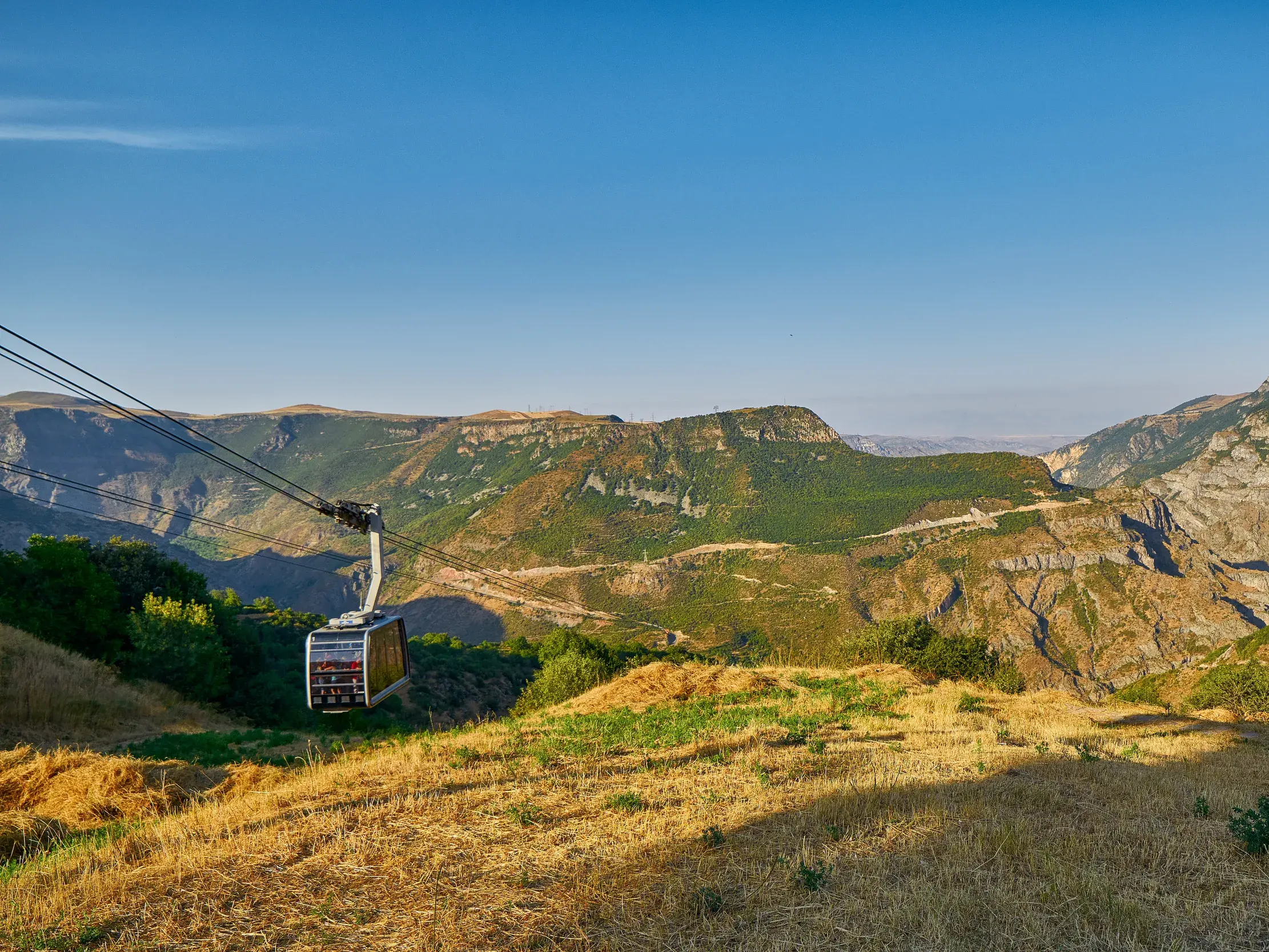 Die Seilbahn "Wings of Tatev" schwebt über die weite, grüne Vorotan-Schlucht in Armenien bei strahlendem Sonnenschein.