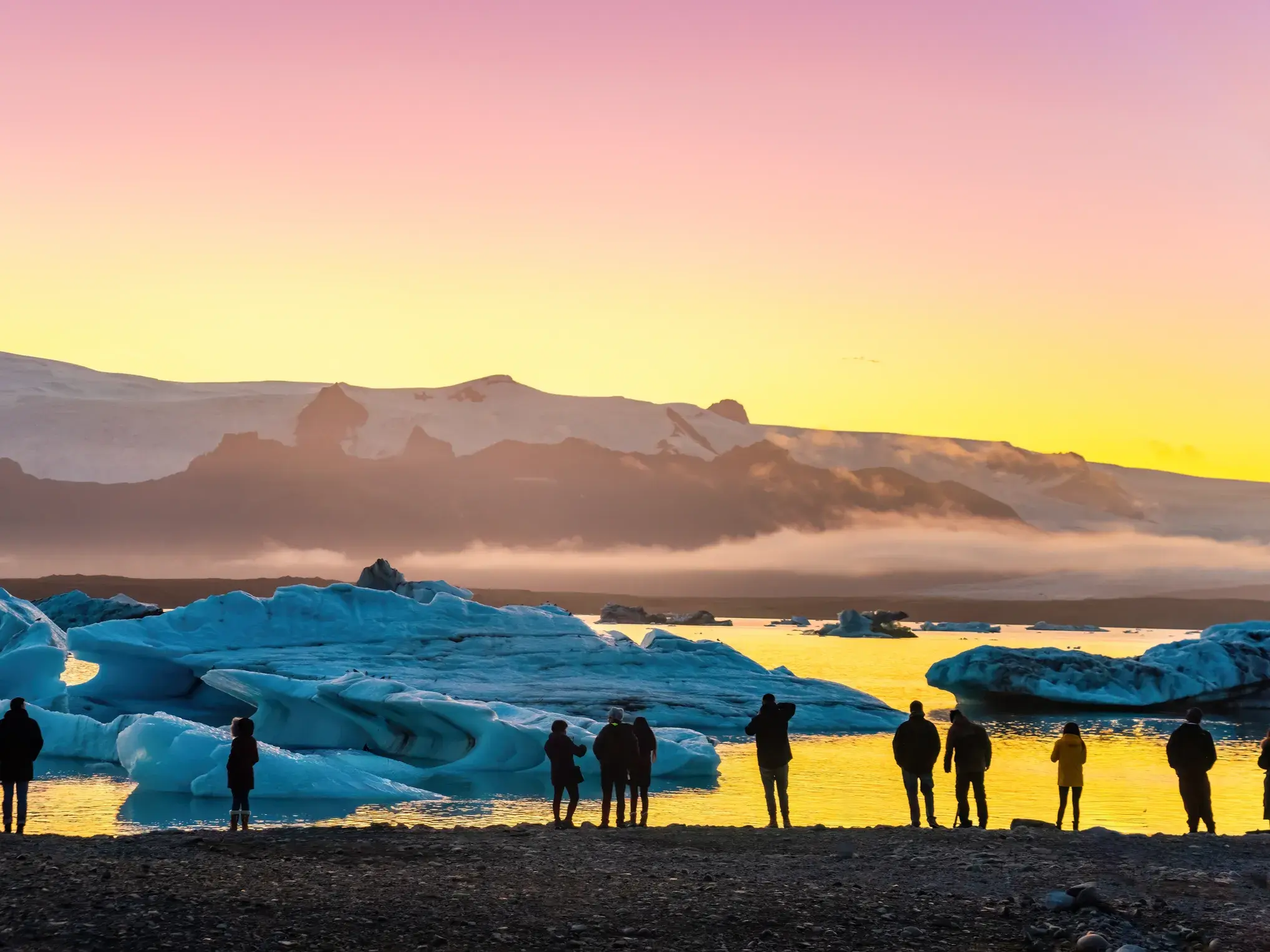 Reisende beobachten bei magischem Abendlicht die Eisberge in der Gletscherlagune Fjallsarlon am Vatnajökull.