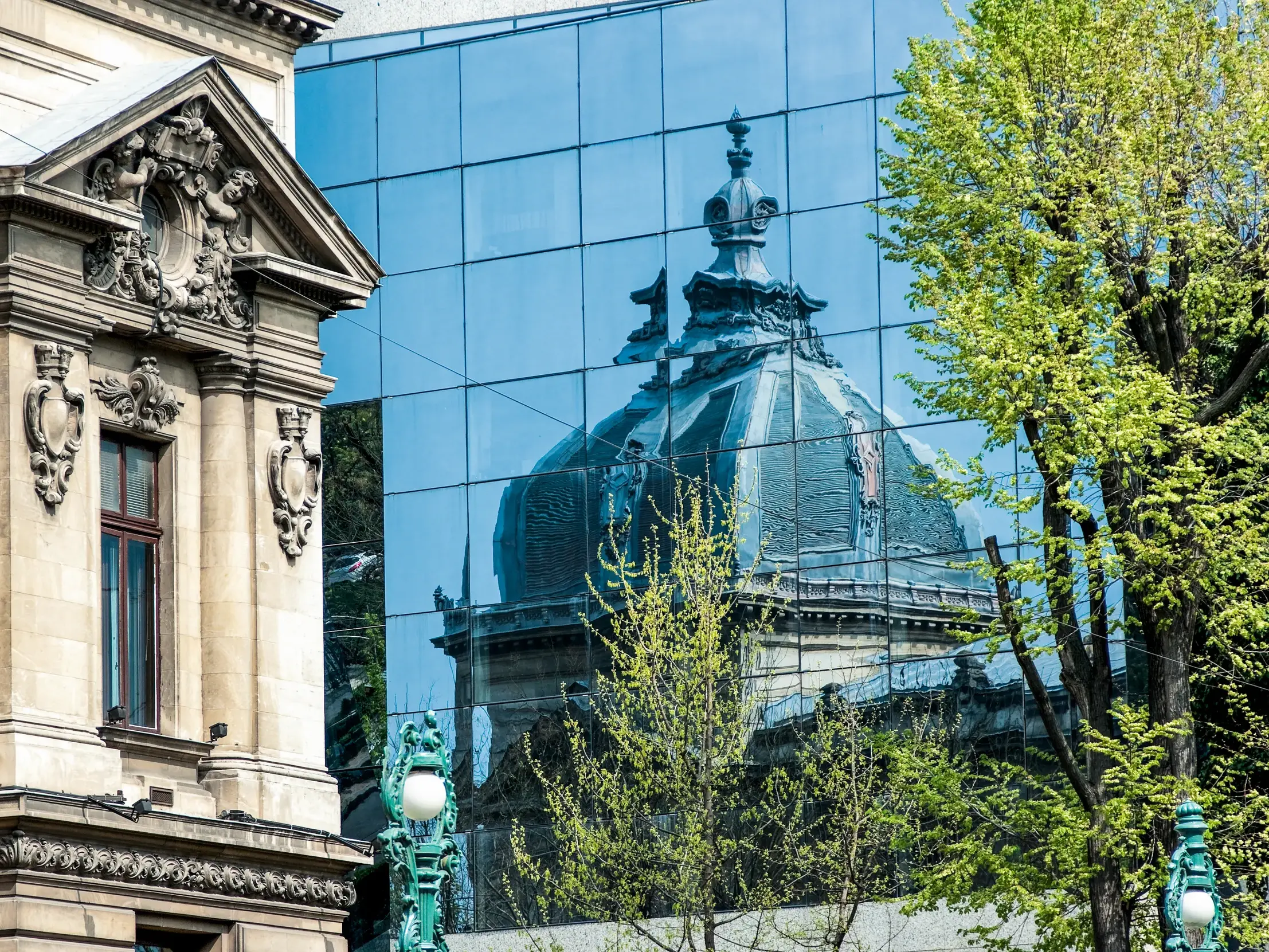 Historische Belle-Epoque-Architektur in Bukarest neben einem modernen Glasbau, der die Kuppel eines Prachtbaus reflektiert.