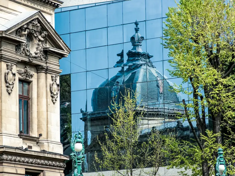 Historische Belle-Epoque-Architektur in Bukarest neben einem modernen Glasbau, der die Kuppel eines Prachtbaus reflektiert.