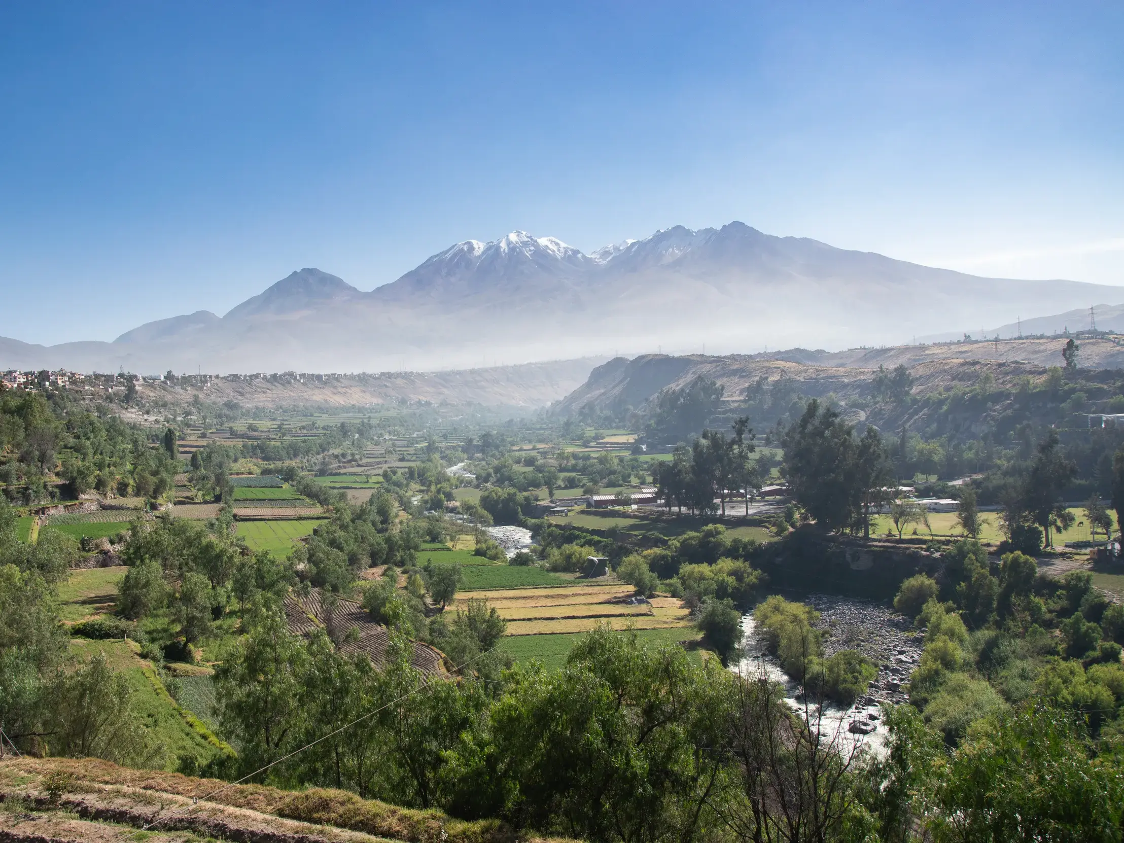 Weitblick einer Wanderreise auf das grüne Chilina-Tal bei Arequipa mit Terrassenfeldern und Vulkanen am Horizont in Peru.