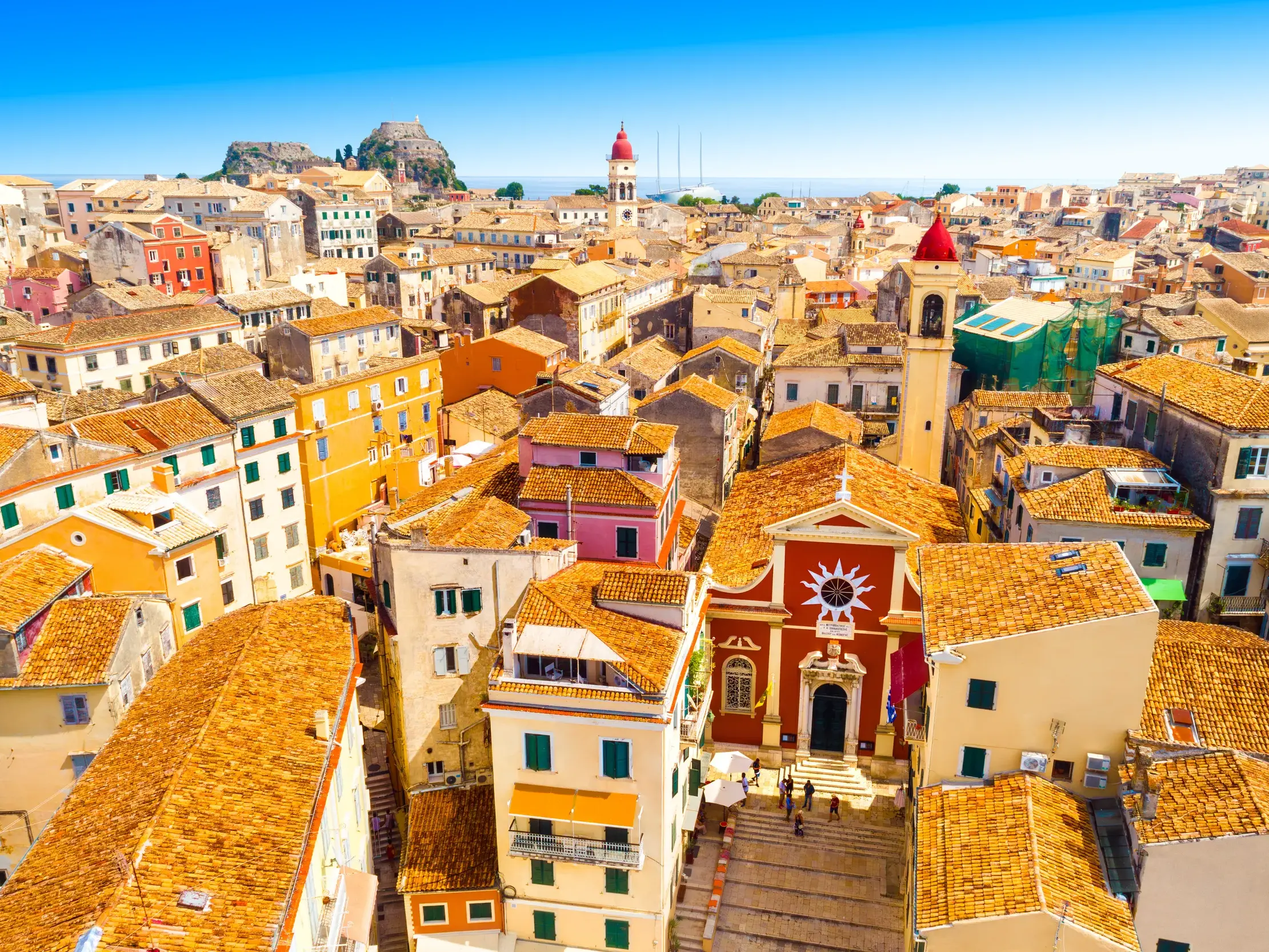 Blick über die bunten Häuser und Ziegeldächer der venezianischen Altstadt von Korfu-Stadt mit einer Kirche am Ionischen Meer.
