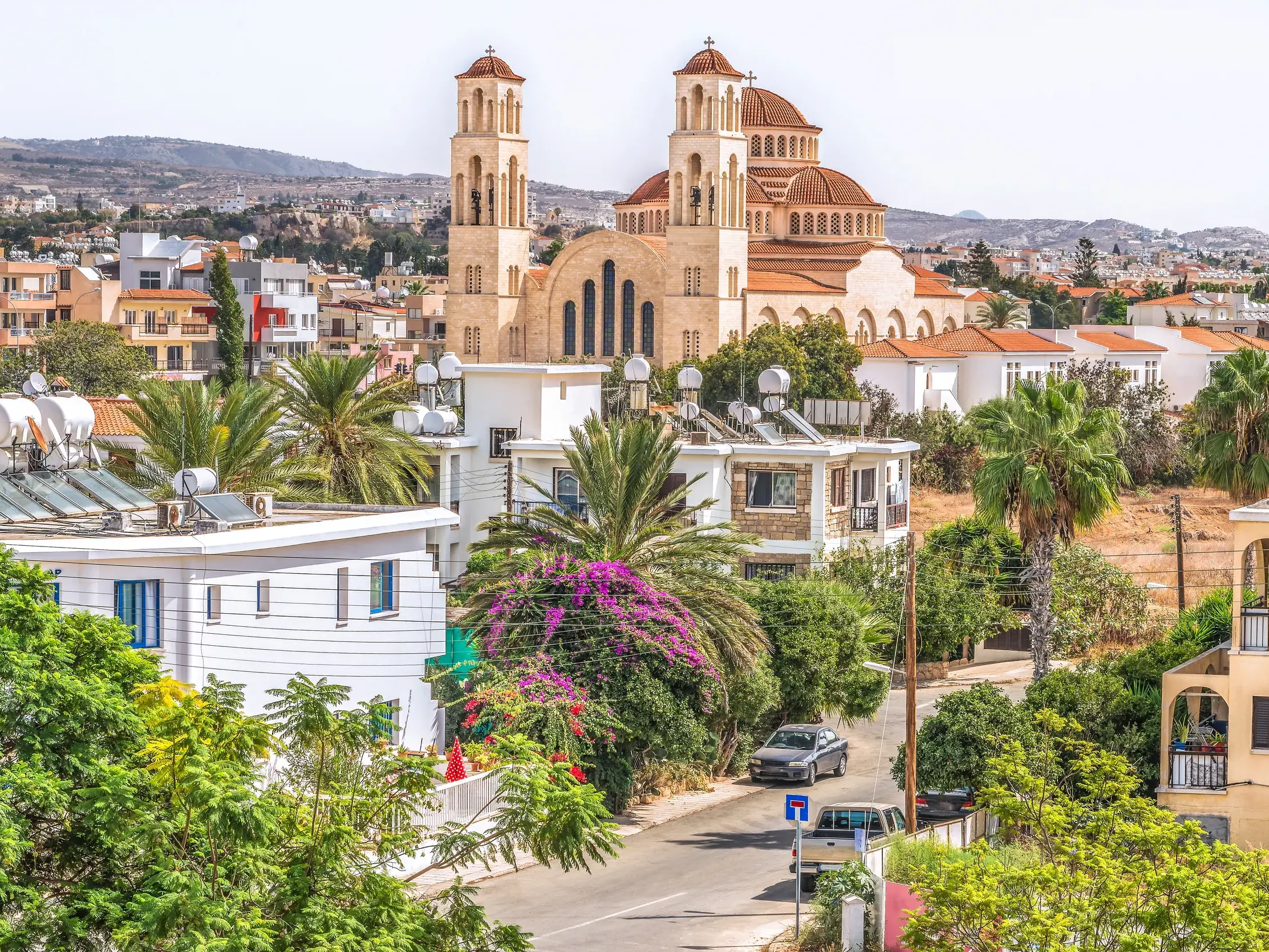 Eine große Kirche mit Kuppel und Türmen thront über den Dächern von Paphos, umgeben von Palmen und mediterranen Häusern.
