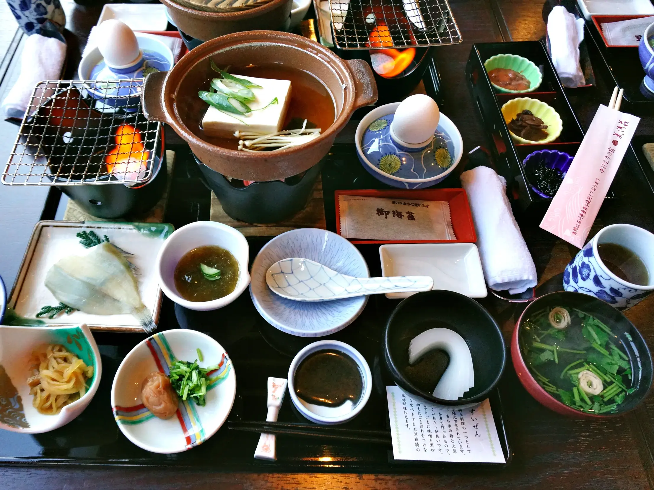 Traditionelles japanisches Abendessen mit vielen kleinen Schalen, Tofu-Suppe im Feuertopf, Reis und Fisch auf einem Tablett.