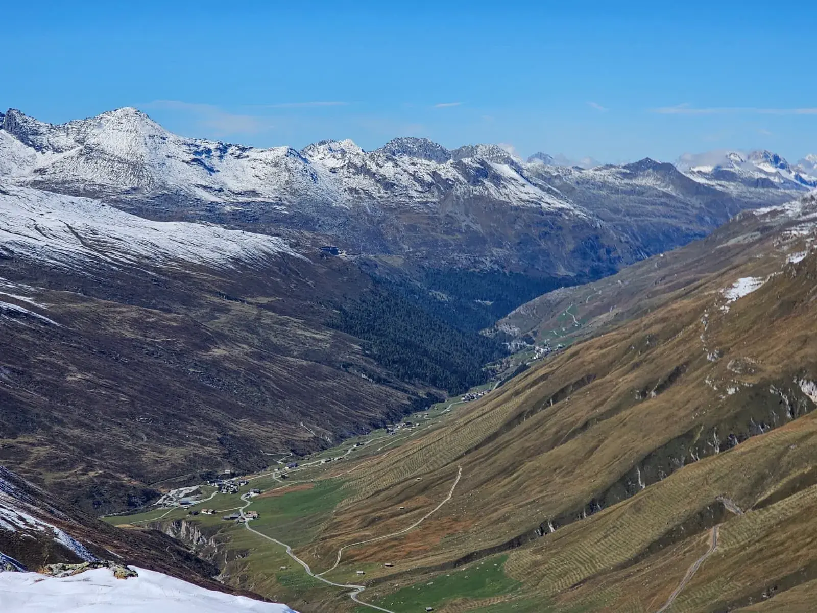 Panoramablick vom Stallerberg auf das tiefgelegene Bergdorf Juf in Graubünden, umgeben von schneebedeckten Alpengipfeln.
