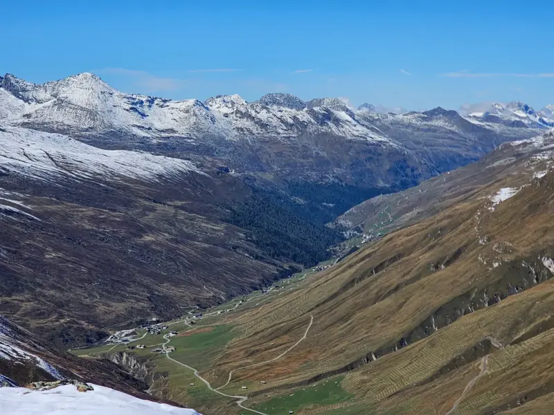 Panoramablick vom Stallerberg auf das tiefgelegene Bergdorf Juf in Graubünden, umgeben von schneebedeckten Alpengipfeln.