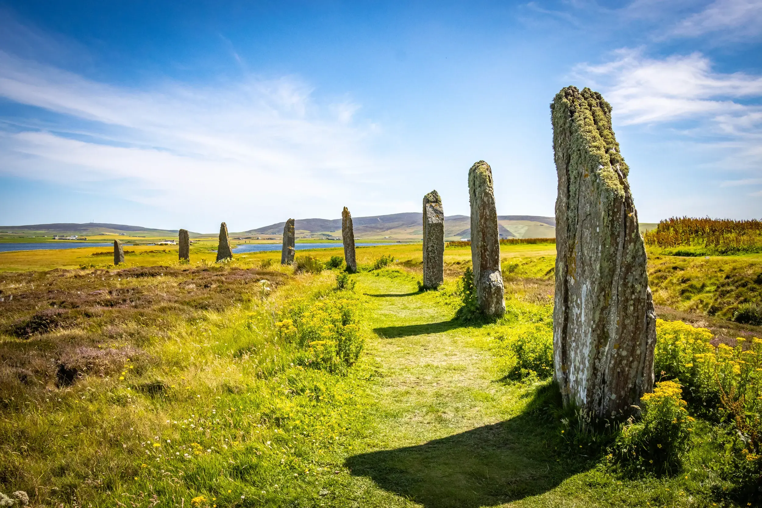 Die prähistorischen, moosbewachsenen Megalithen des Ring of Brodgar auf den Orkneys unter blauem Himmel in Schottland.