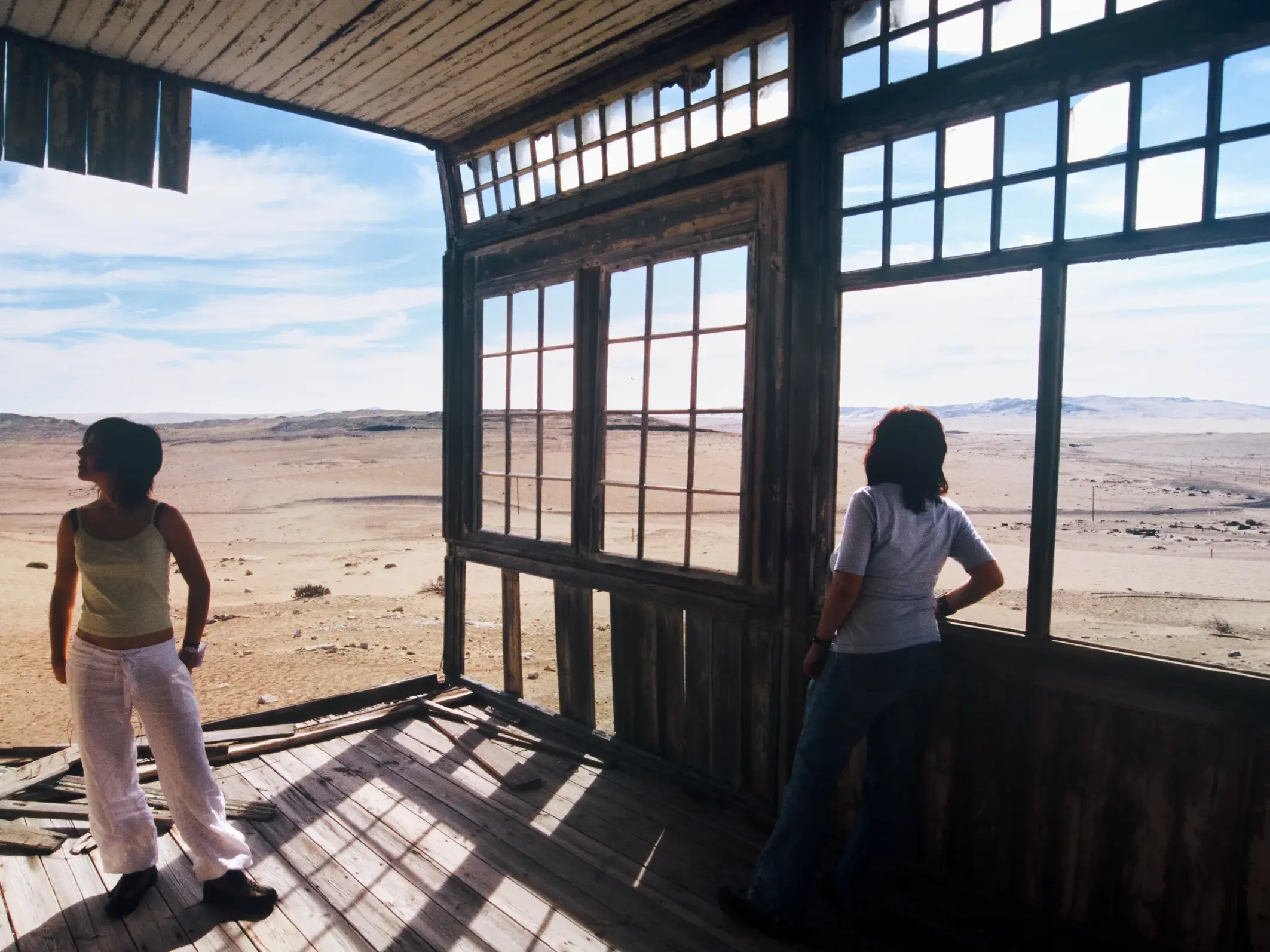Zwei Frauen auf einer Studienreise blicken aus einem verfallenen Haus in der Geisterstadt Kolmanskuppe auf die Namib-Wüste.