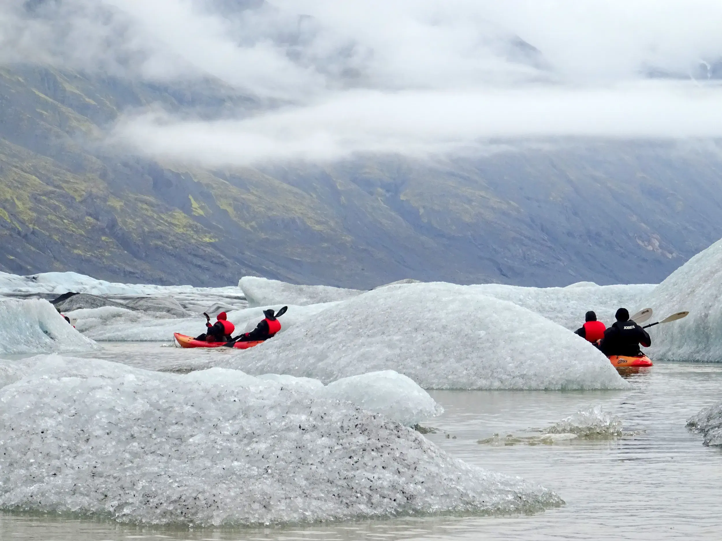 Eine kleine Reisegruppe bei einer Kajak-Tour durch die beeindruckenden Eisberge der Gletscherlagune Jökulsárlón in Island.