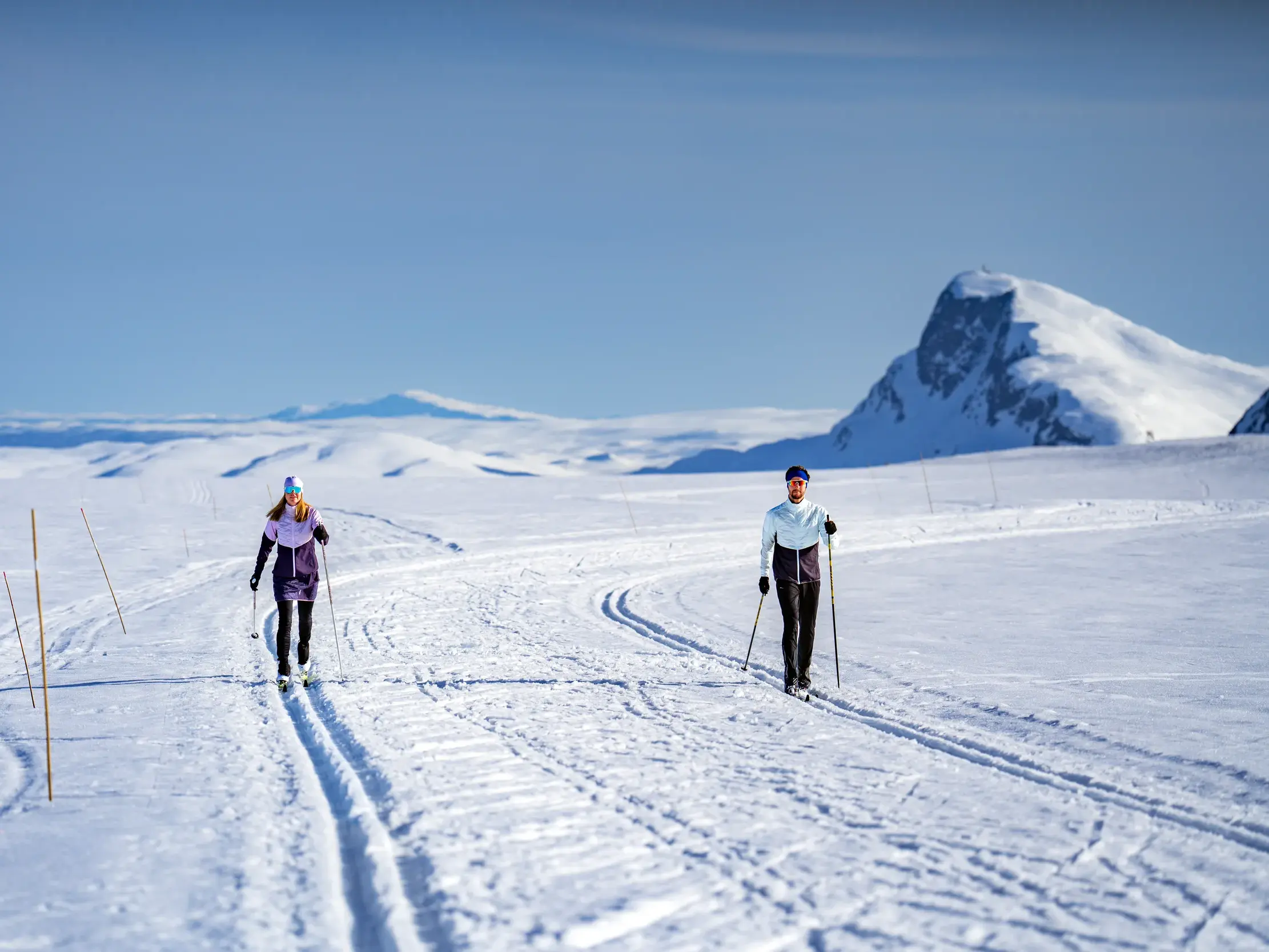 Zwei Langläufer auf einer Loipe in der weiten, sonnigen Schneelandschaft von Valdres mit Blick auf die Berge Norwegens.