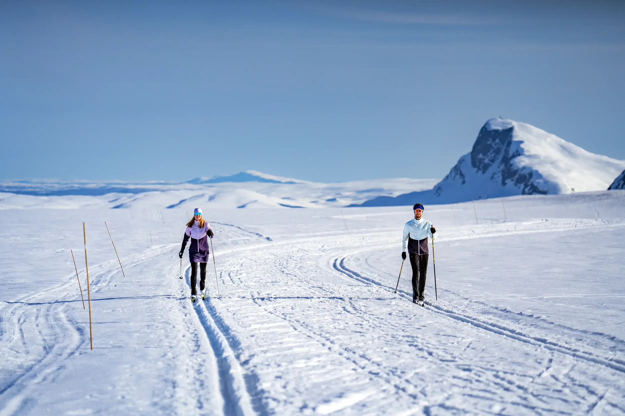 Zwei Langläufer auf einer Loipe in der weiten, sonnigen Schneelandschaft von Valdres mit Blick auf die Berge Norwegens.
