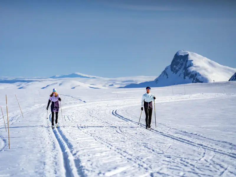 Zwei Langläufer auf einer Loipe in der weiten, sonnigen Schneelandschaft von Valdres mit Blick auf die Berge Norwegens.