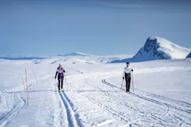 Zwei Langläufer auf einer Loipe in der weiten, sonnigen Schneelandschaft von Valdres mit Blick auf die Berge Norwegens.