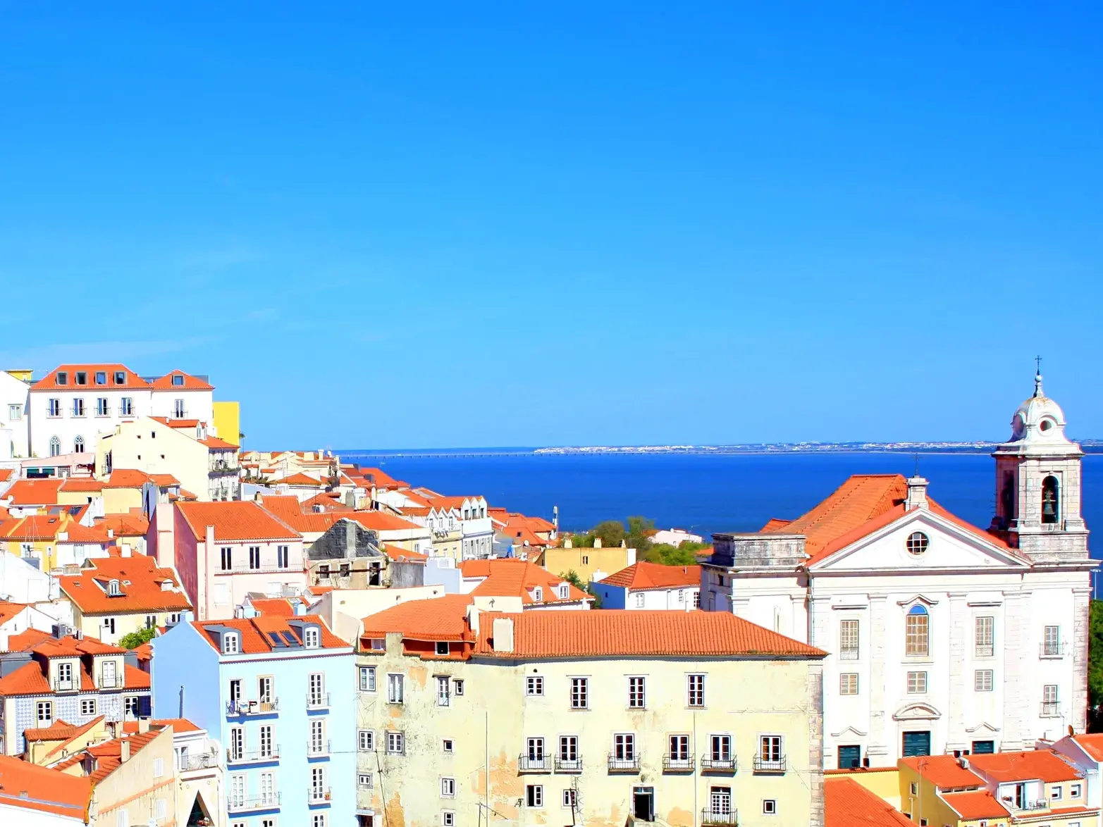 Sonniger Blick über die bunten Fassaden und roten Ziegeldächer der Altstadt Alfama in Lissabon zum weiten, blauen Meer.