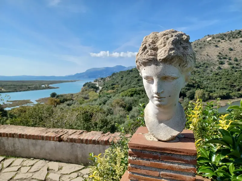Antike Steinbüste auf einer Mauer im UNESCO-Weltkulturerbe Butrint mit Panoramablick über die Albanische Riviera.