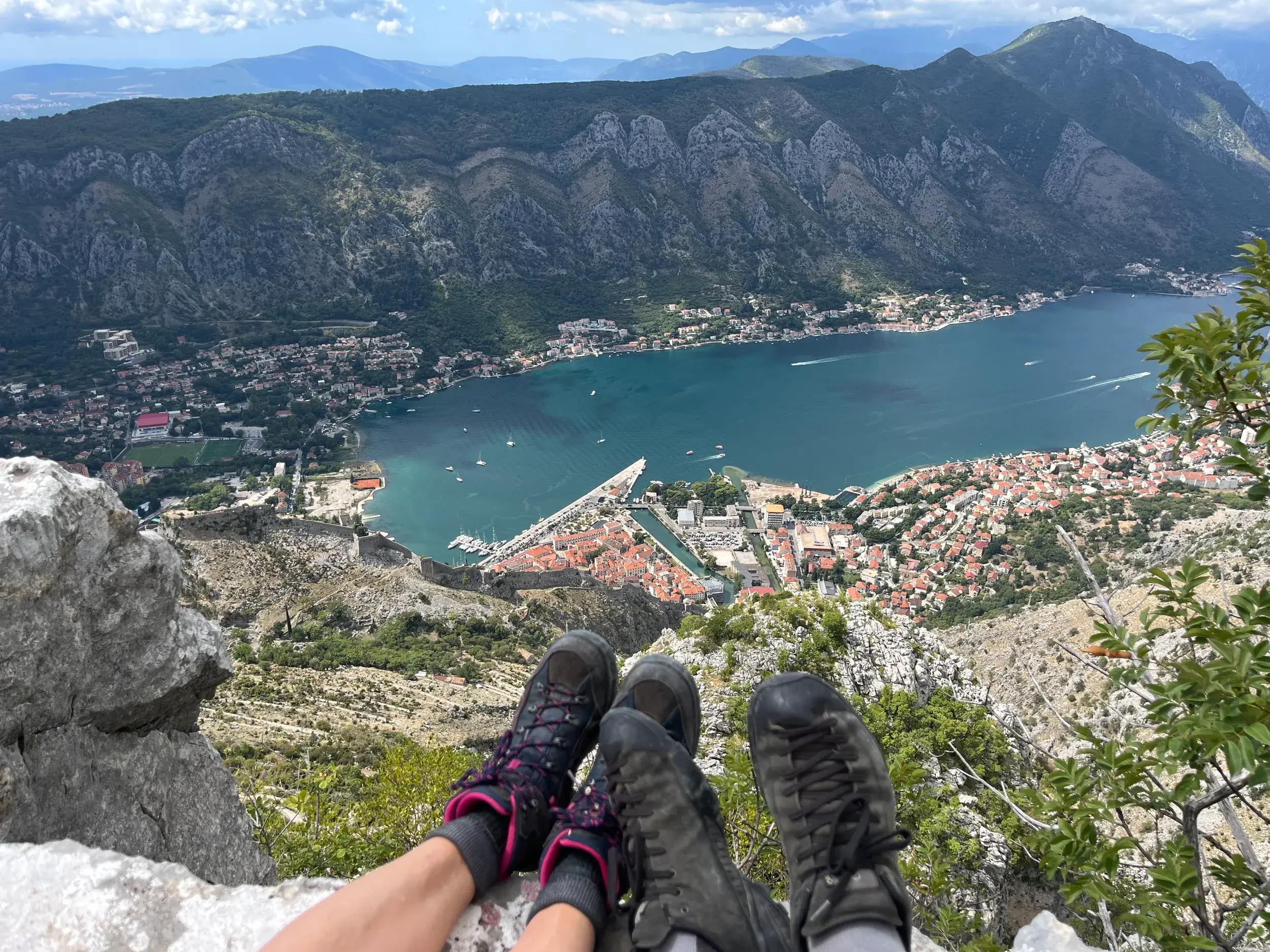 Zwei Wanderer machen Pause mit Panoramablick von einem Berg auf die historische Altstadt und die fjordartige Bucht von Kotor.