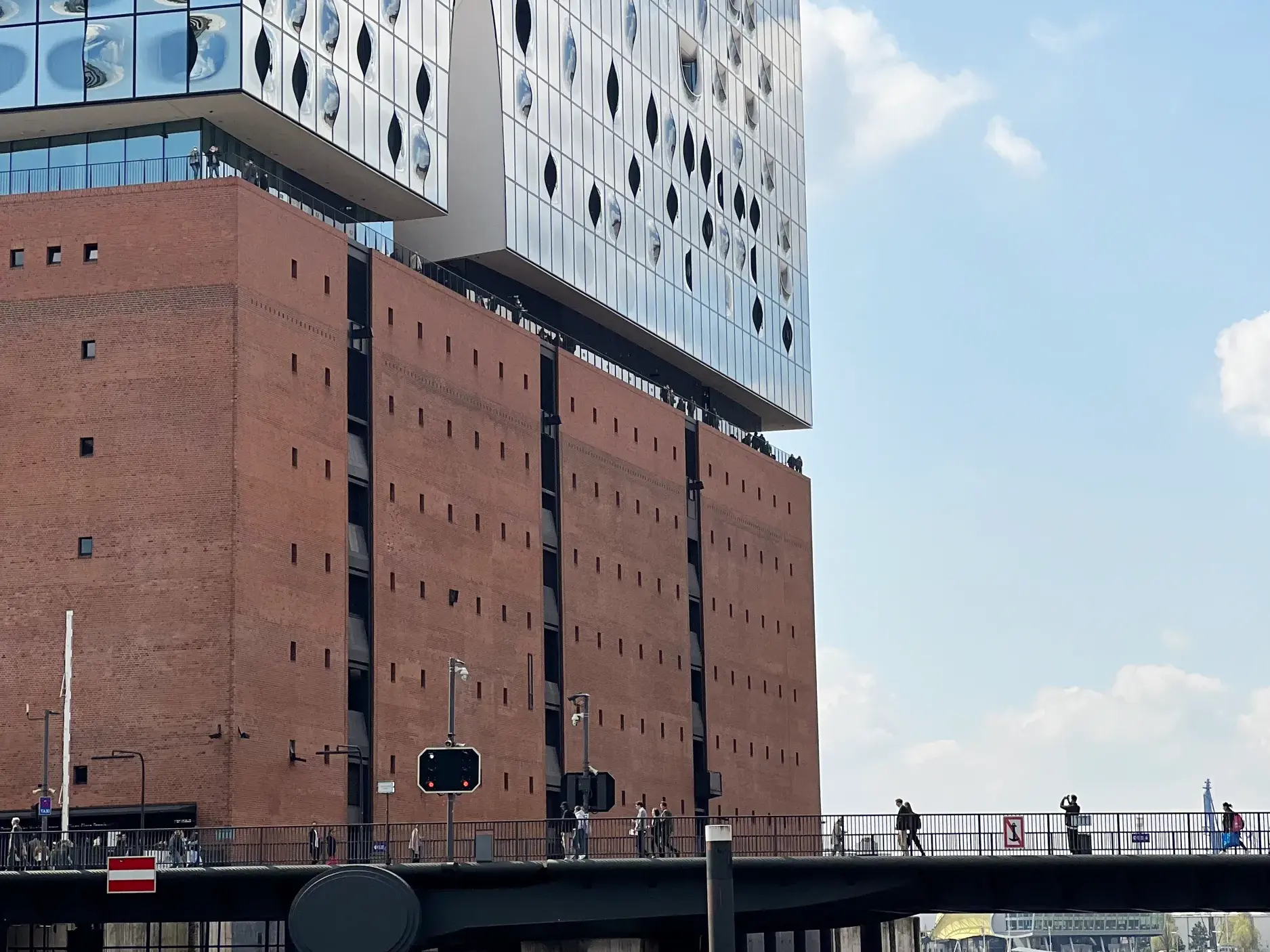 Backsteinsockel und Glasfassade der Elbphilharmonie in Hamburg mit Fußgängerbrücke davor