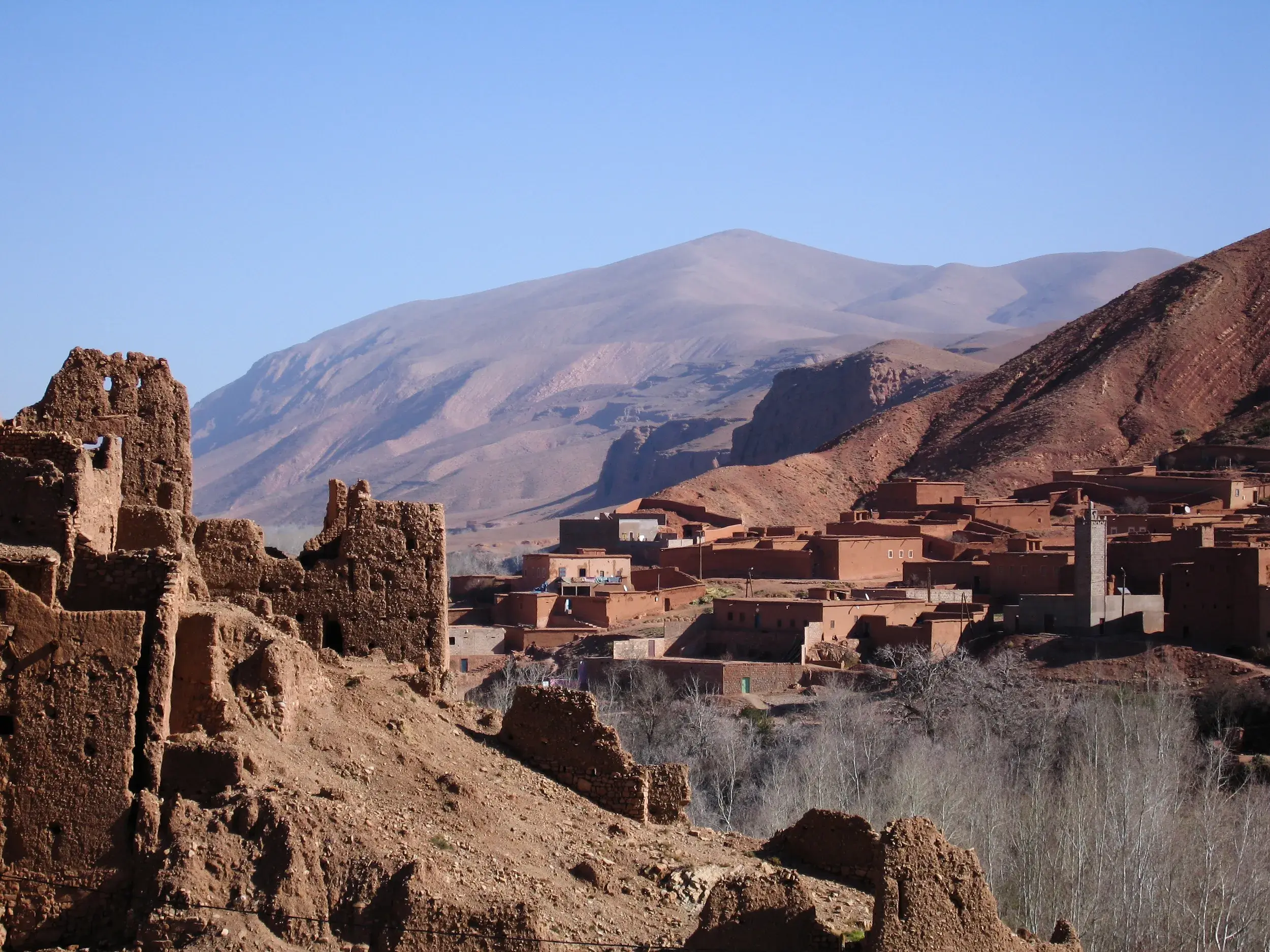 Ockerfarbene Lehmburgen und Kasbah-Ruinen im Dades-Tal, im Hintergrund die karge Berglandschaft des Atlasgebirges Marokkos.