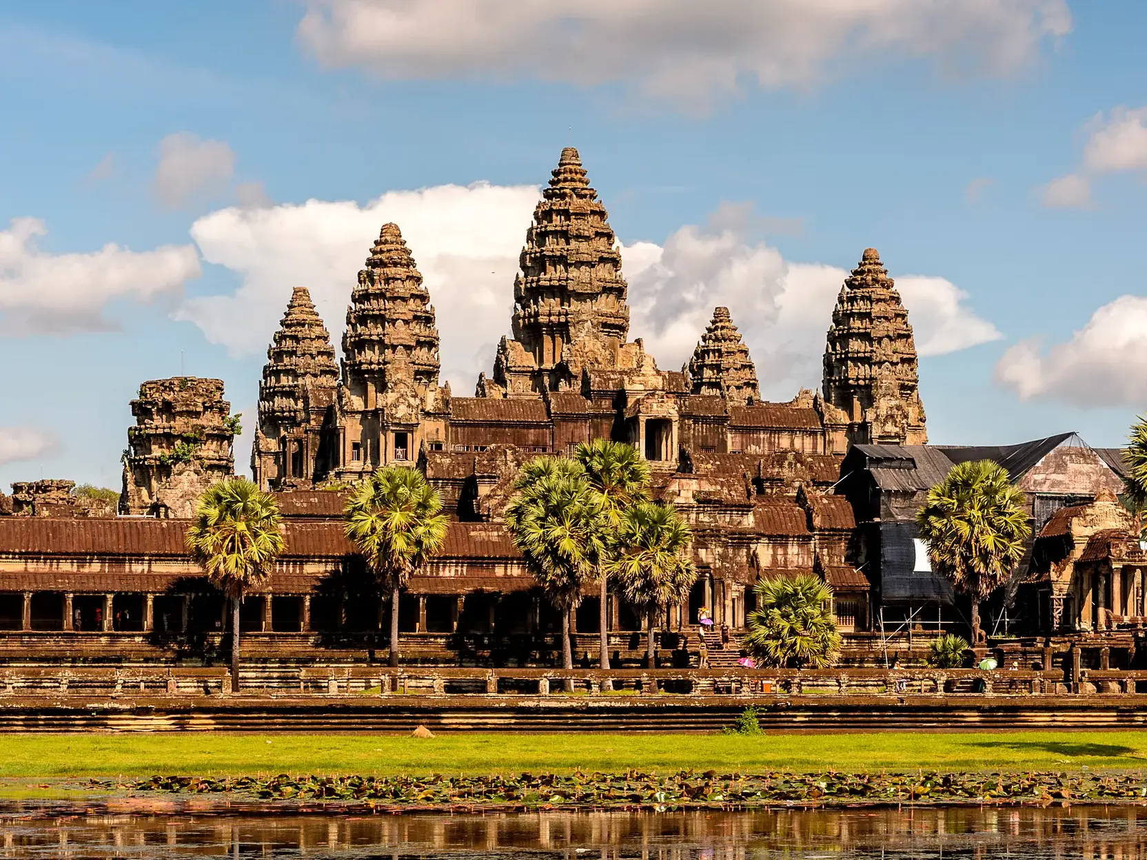 Die majestätische Tempelanlage von Angkor Wat in Kambodscha mit ihren fünf markanten Türmen hinter Palmen und Wassergraben.