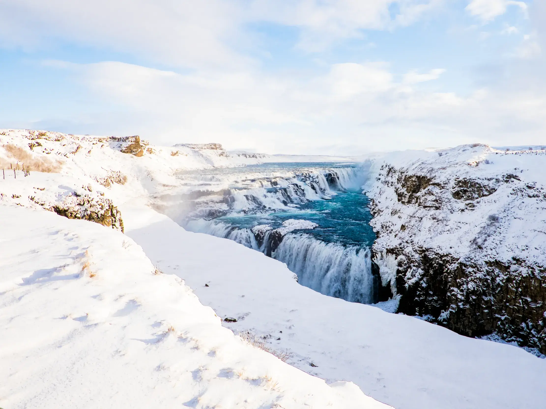 Türkisfarbenes Wasser des Gullfoss Wasserfalls stürzt in eine tiefe, schneebedeckte Schlucht in der Winterlandschaft Islands.